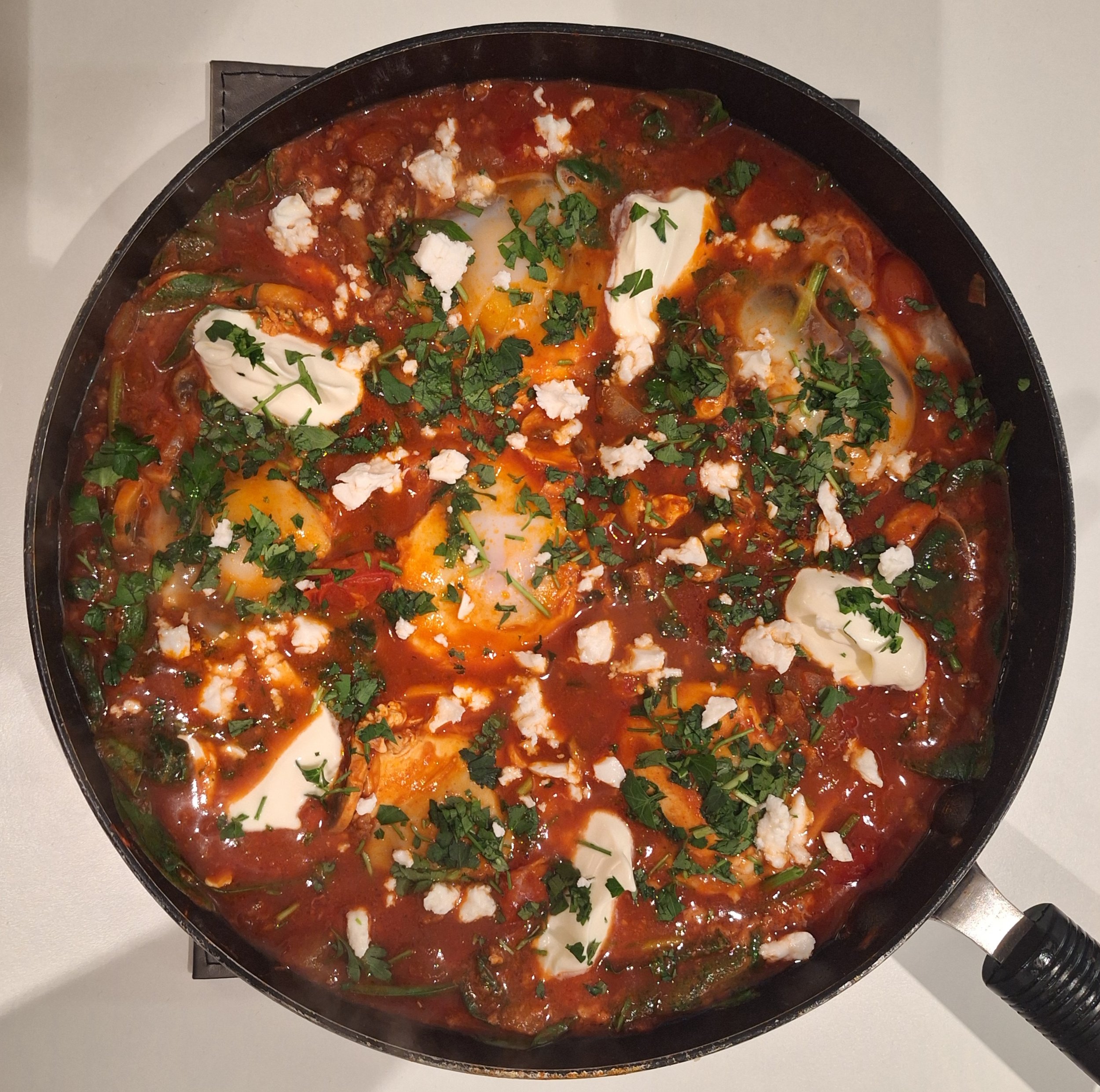 Shakshuka in a black skillet with eggs, tomato sauce, herbs, and cheese.