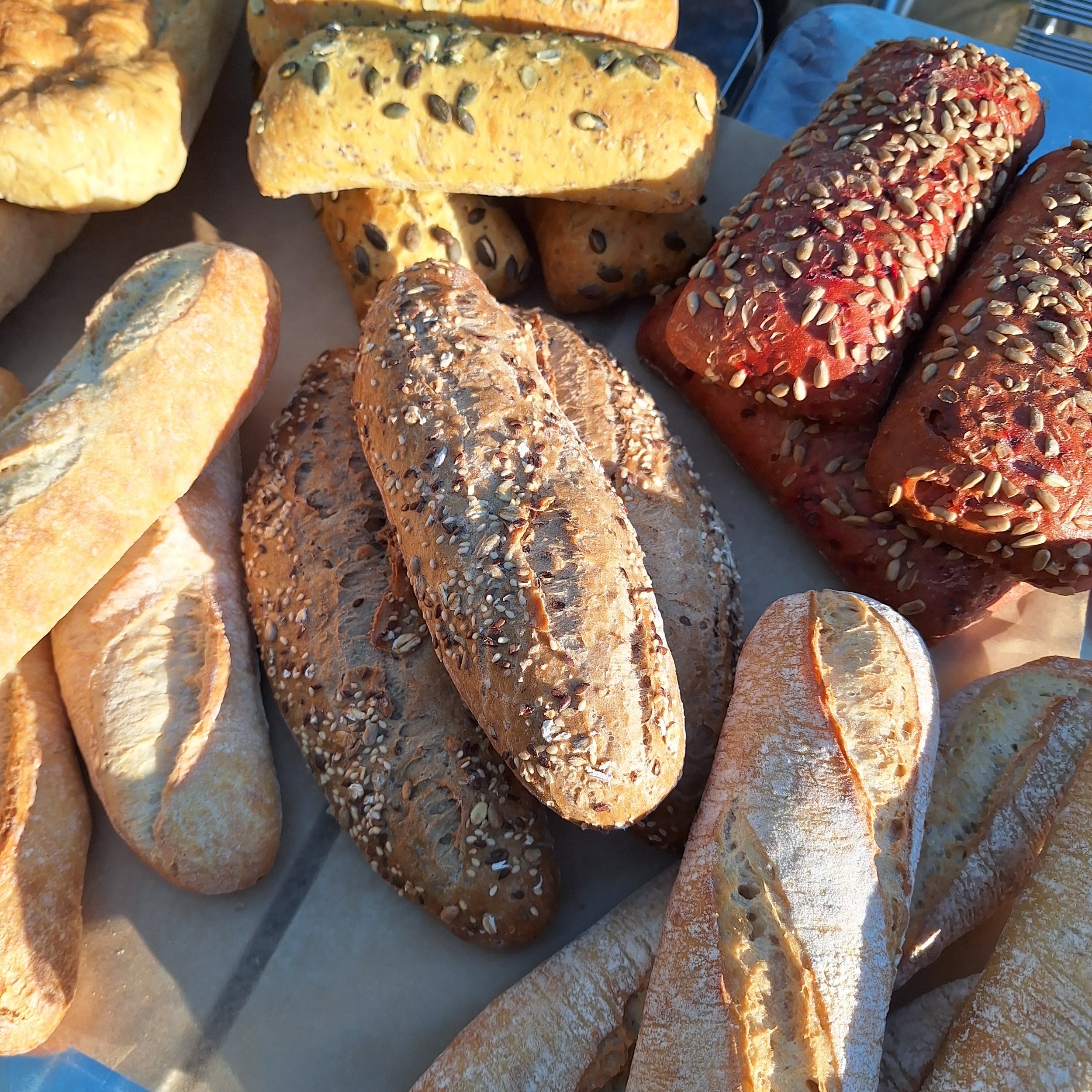 Assorted loaves of bread, including baguettes, multigrain, and seeded rolls displayed on a surface.