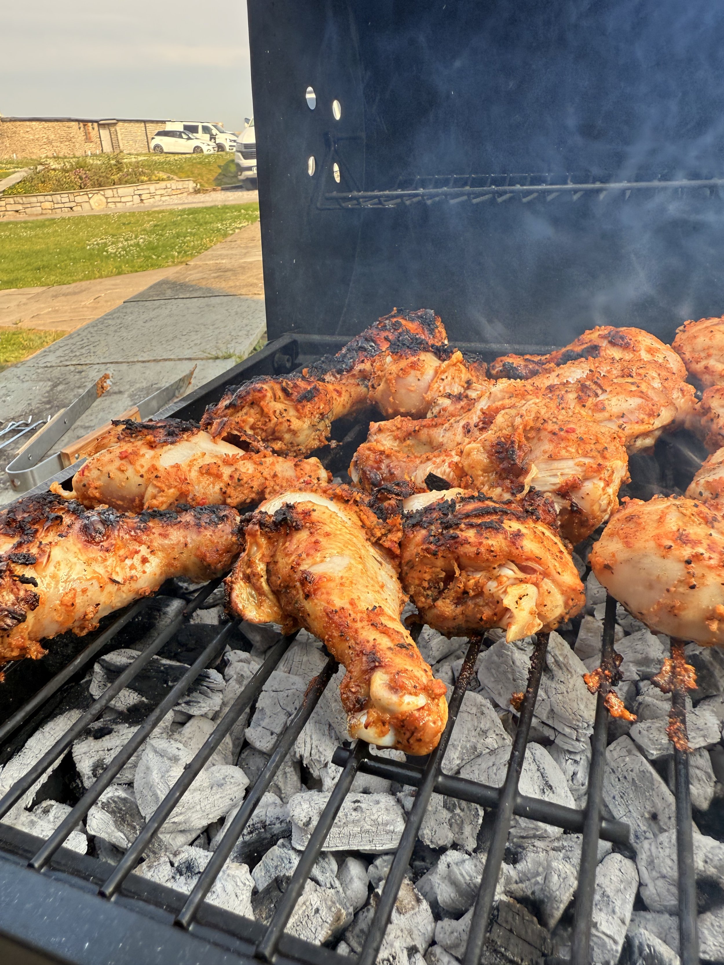 Chicken pieces grilling on a barbecue grill with charcoal, outdoors on a sunny day.