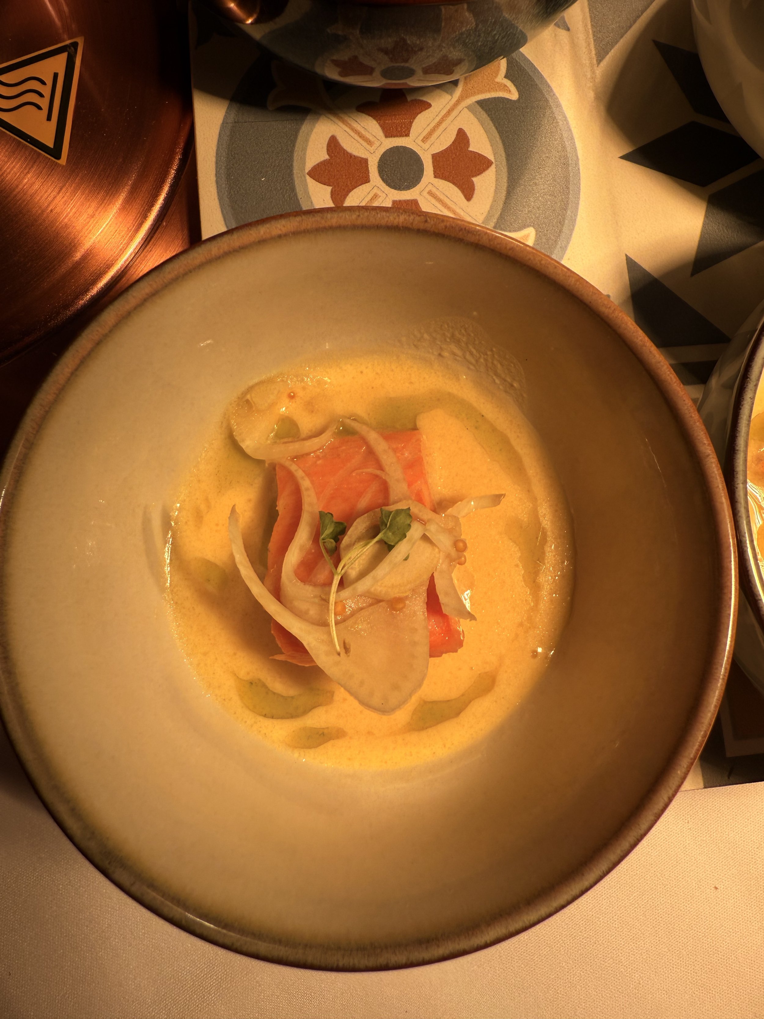 A bowl of seafood ceviche with sliced onions and microgreens, served with a yellow citrus sauce.