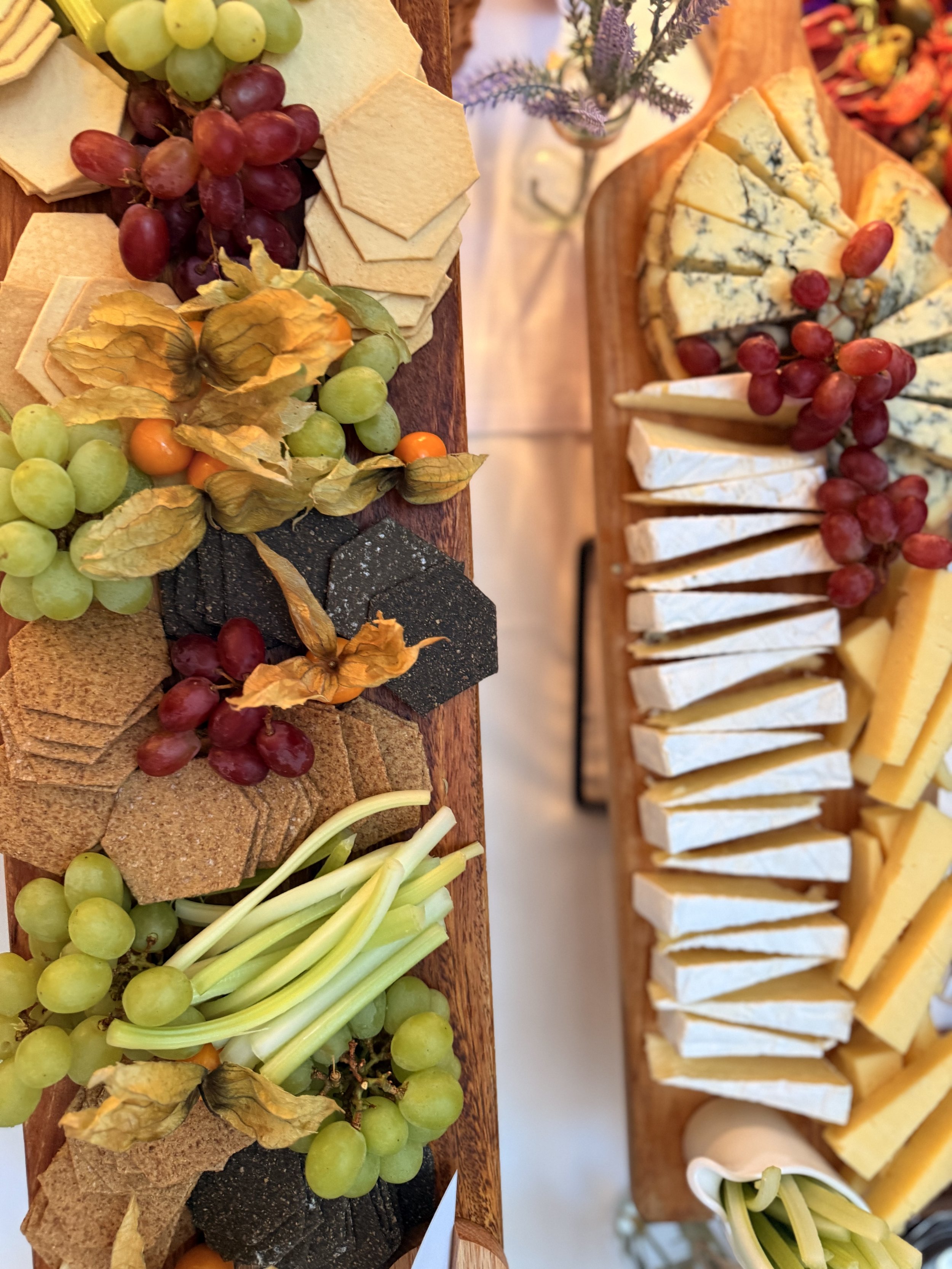 Assorted cheeses, grapes, dried physalis, crackers, and vegetables on wooden trays at a cheese board.