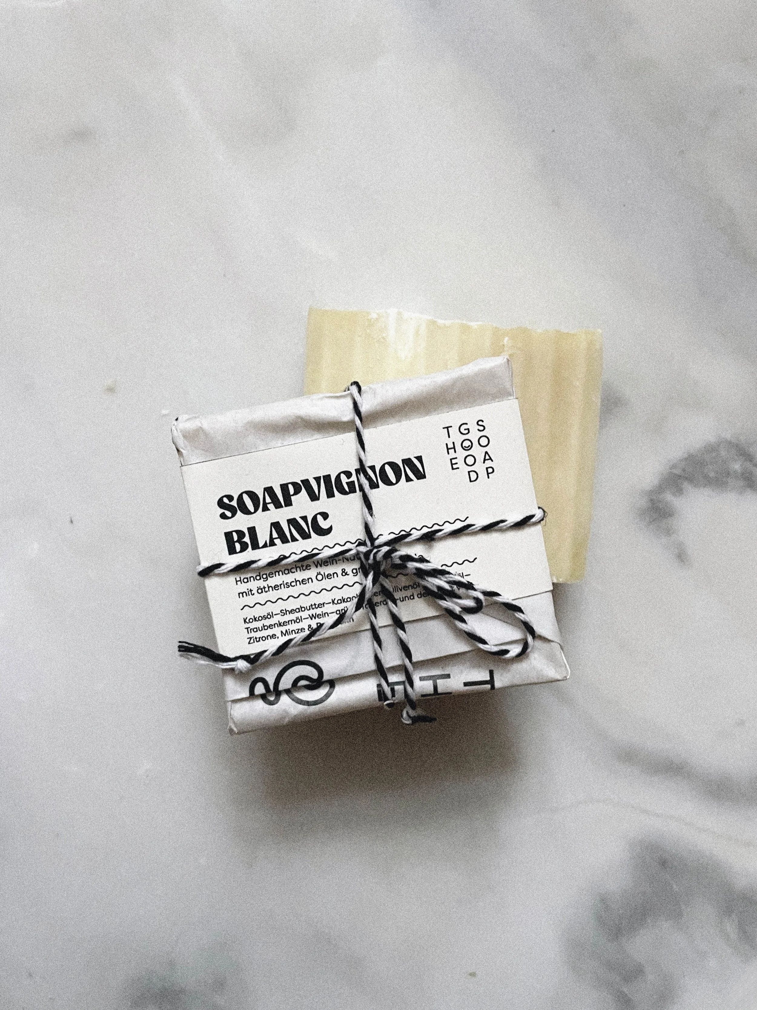 Ein handgemachtes Seifenstück, eingewickelt in Papier mit schwarzen und weißen Kordeln, auf einer weißen Oberfläche.