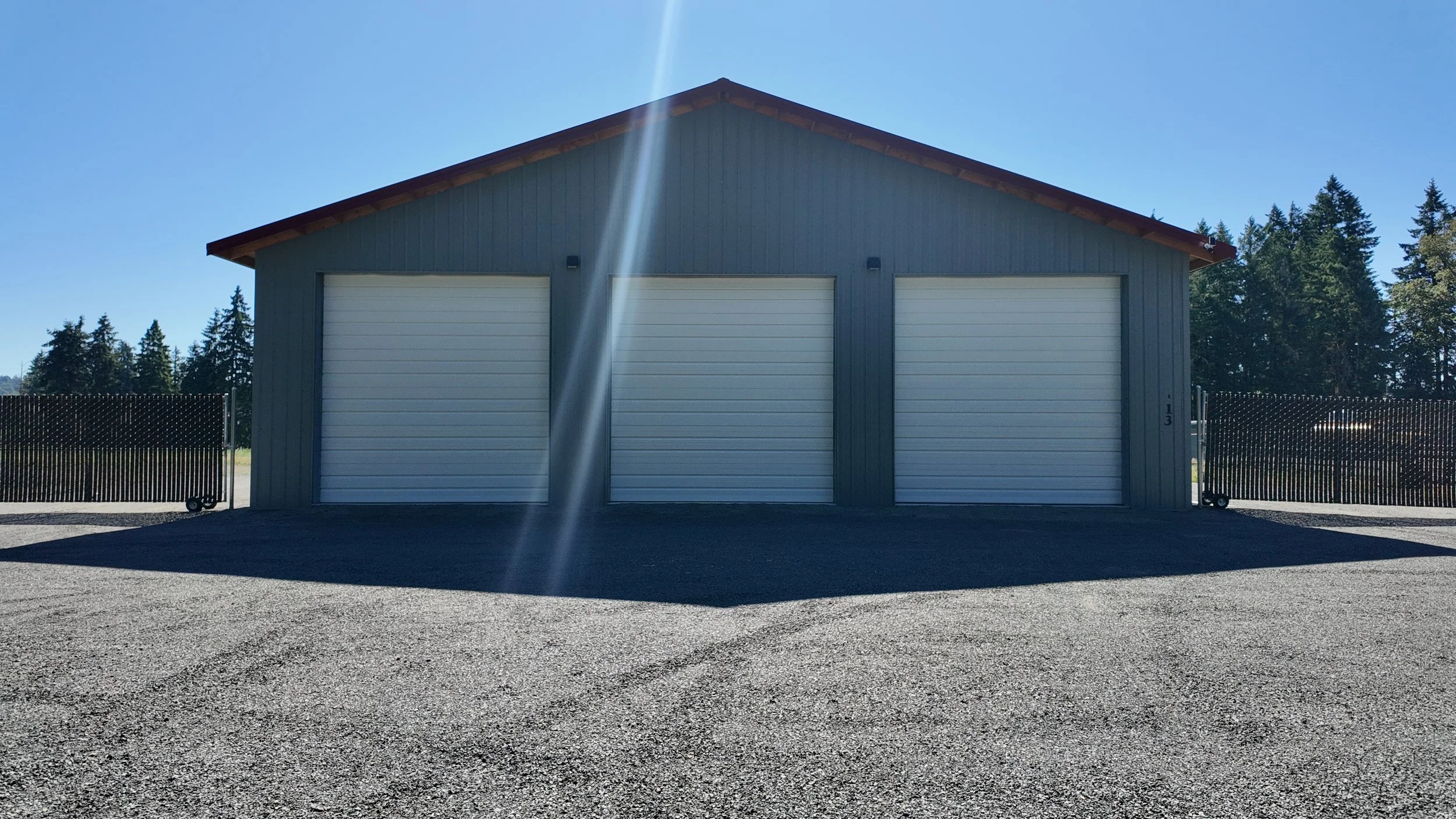 Finished custom Columbia Structure pole barn shop with gray steel siding and three white roll-up garage doors in Southwest Washington