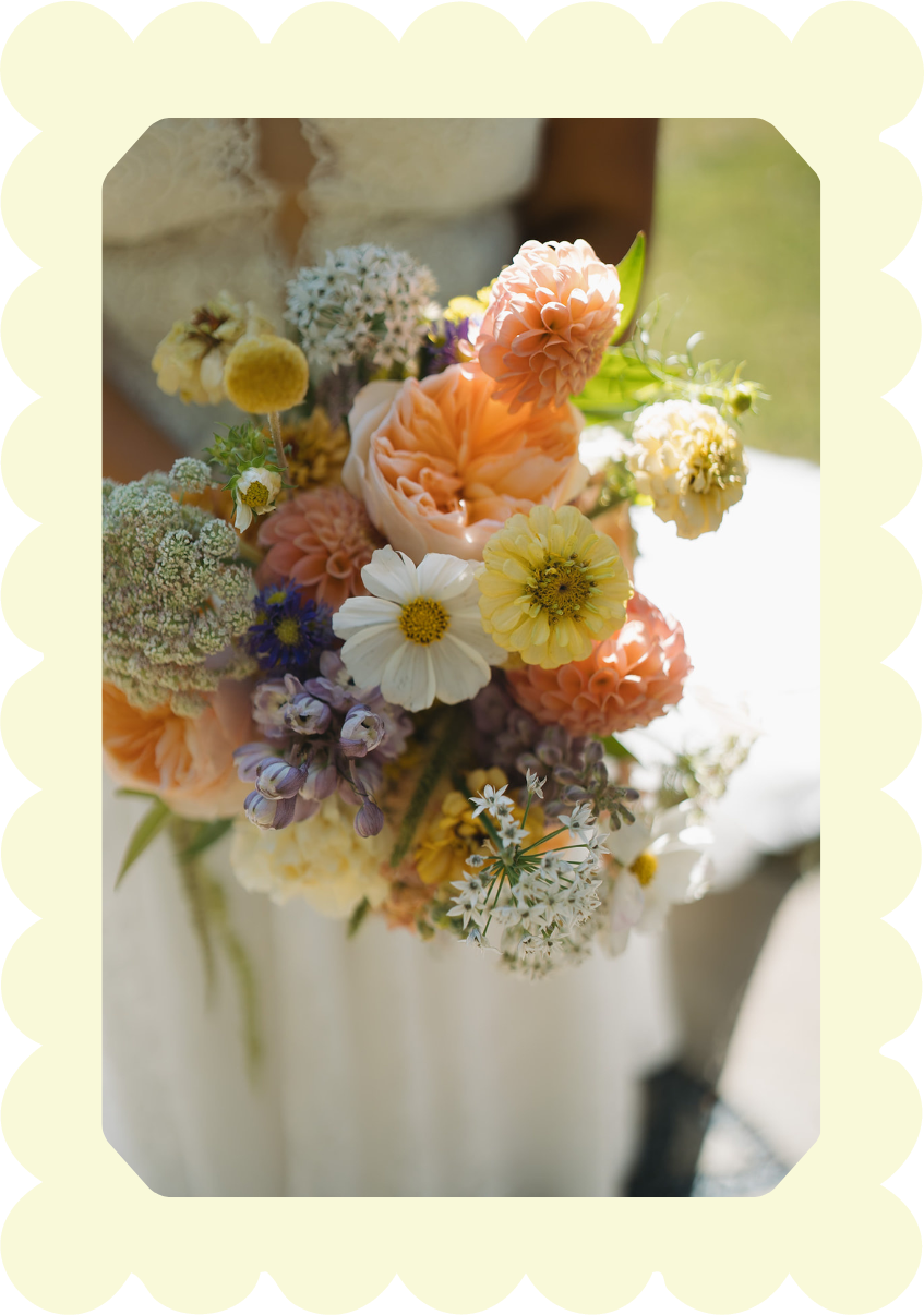 A person holding a bouquet of mixed flowers, including peonies, daisies, and other colorful blooms, in natural light.