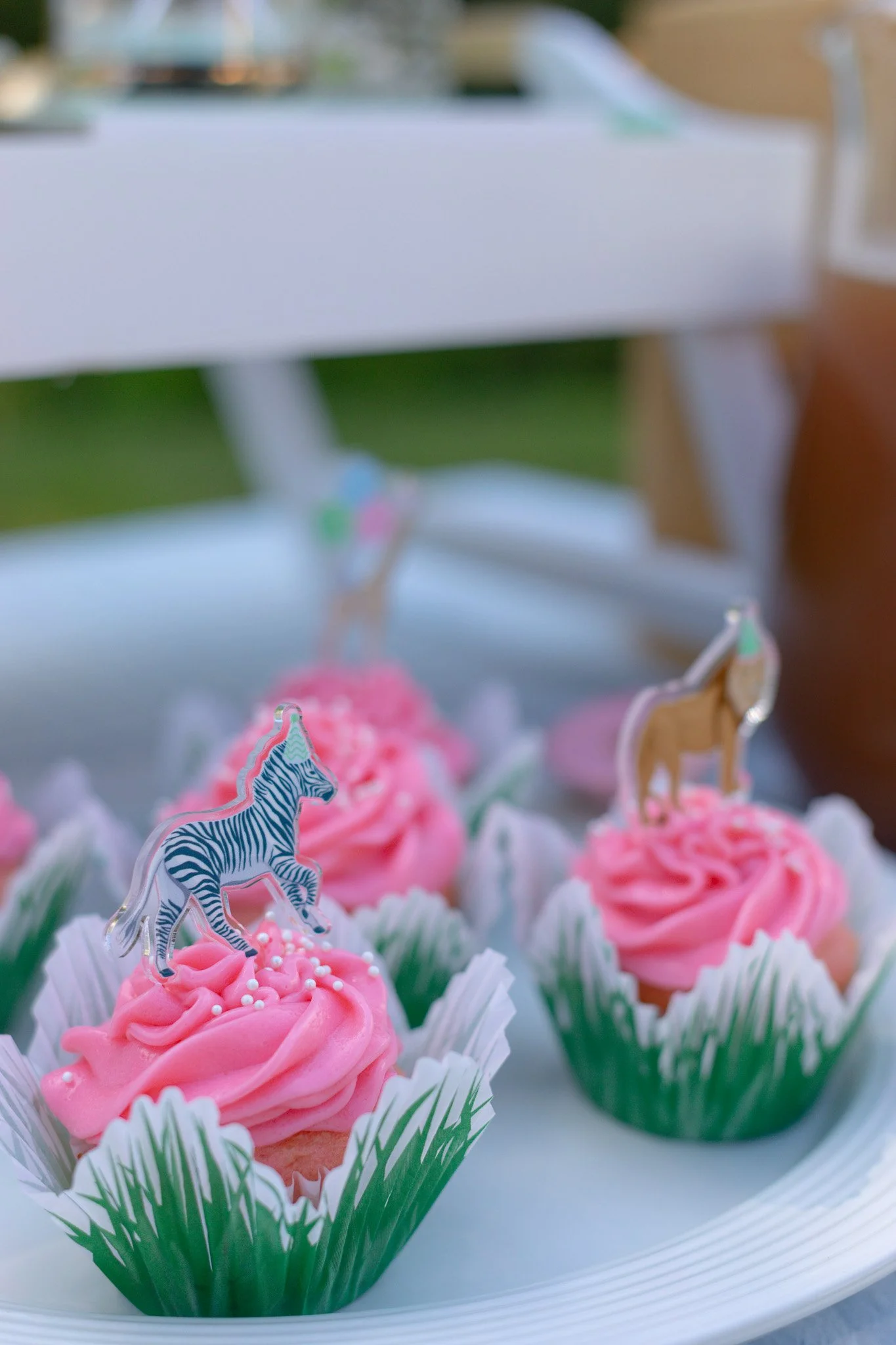 Pink cupcakes decorated with zebra and lion toppers and white sprinkles on a white plate.