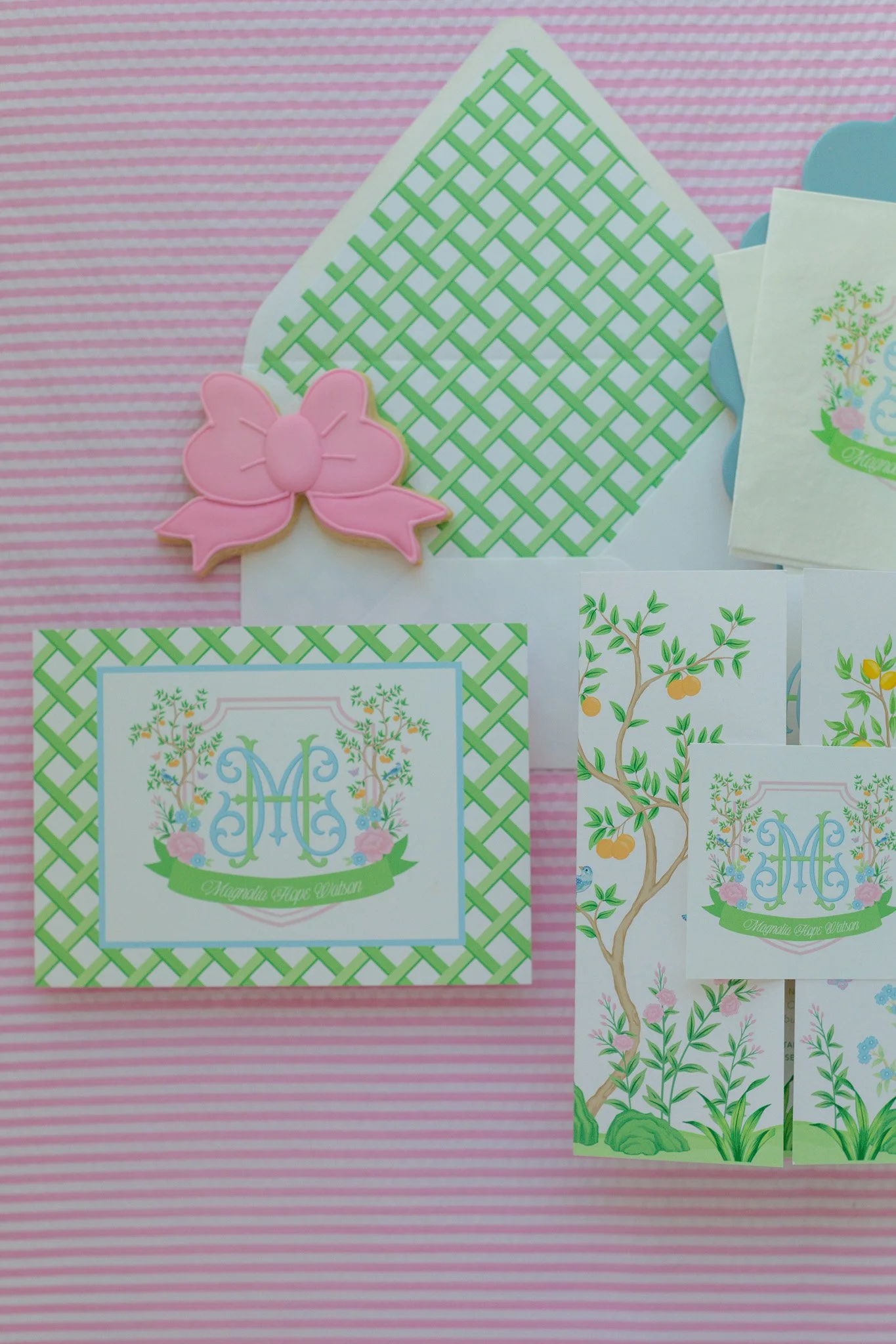 Spring-themed stationery with floral and fruit motifs, labeled with the name Magnolia Page Watson, including a pink bow-shaped eraser, decorative envelopes, and patterned cards on a pink striped background.