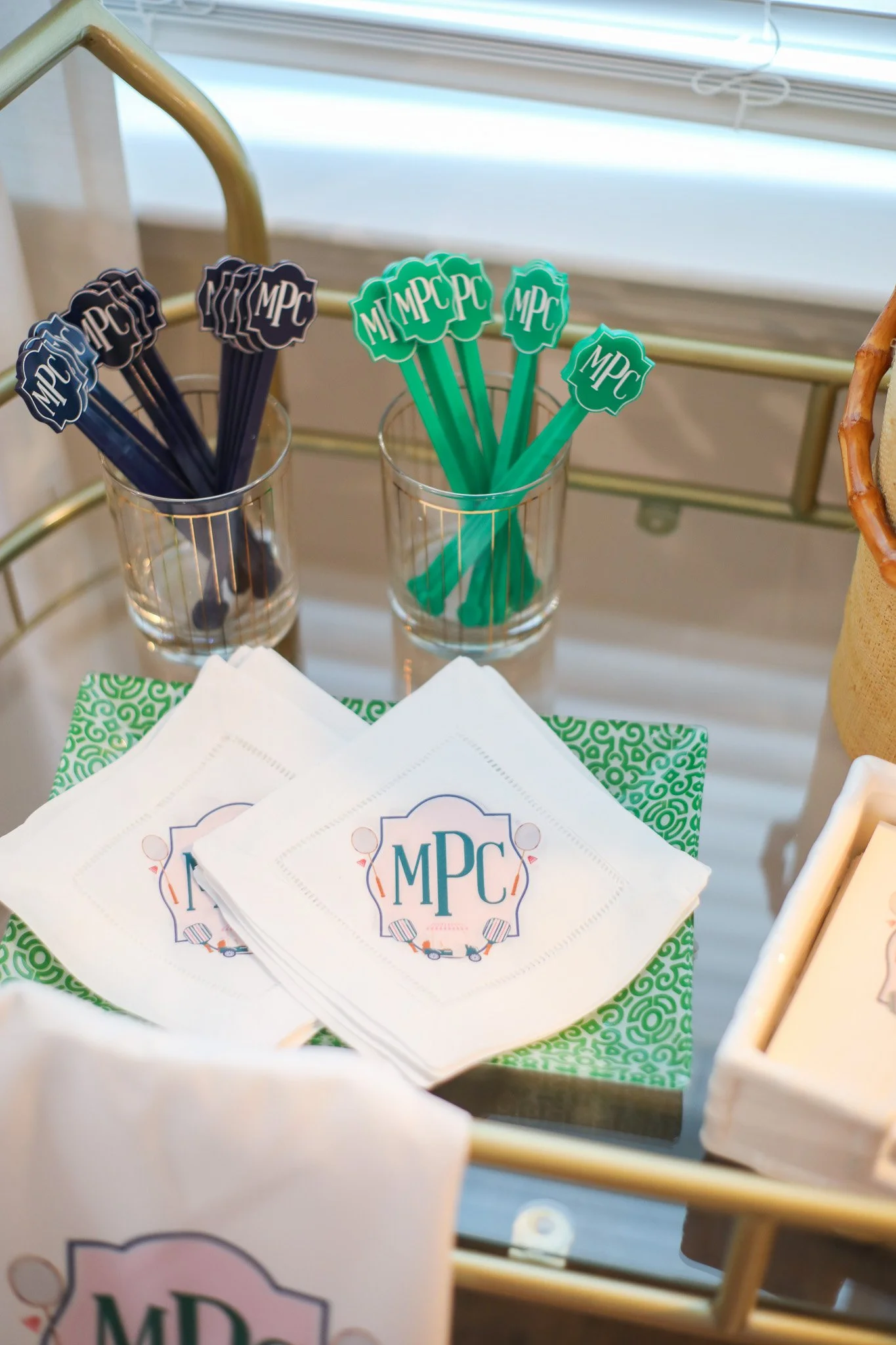 Party supplies featuring napkins and stir sticks with the initials MPC, arranged on a table near a window.