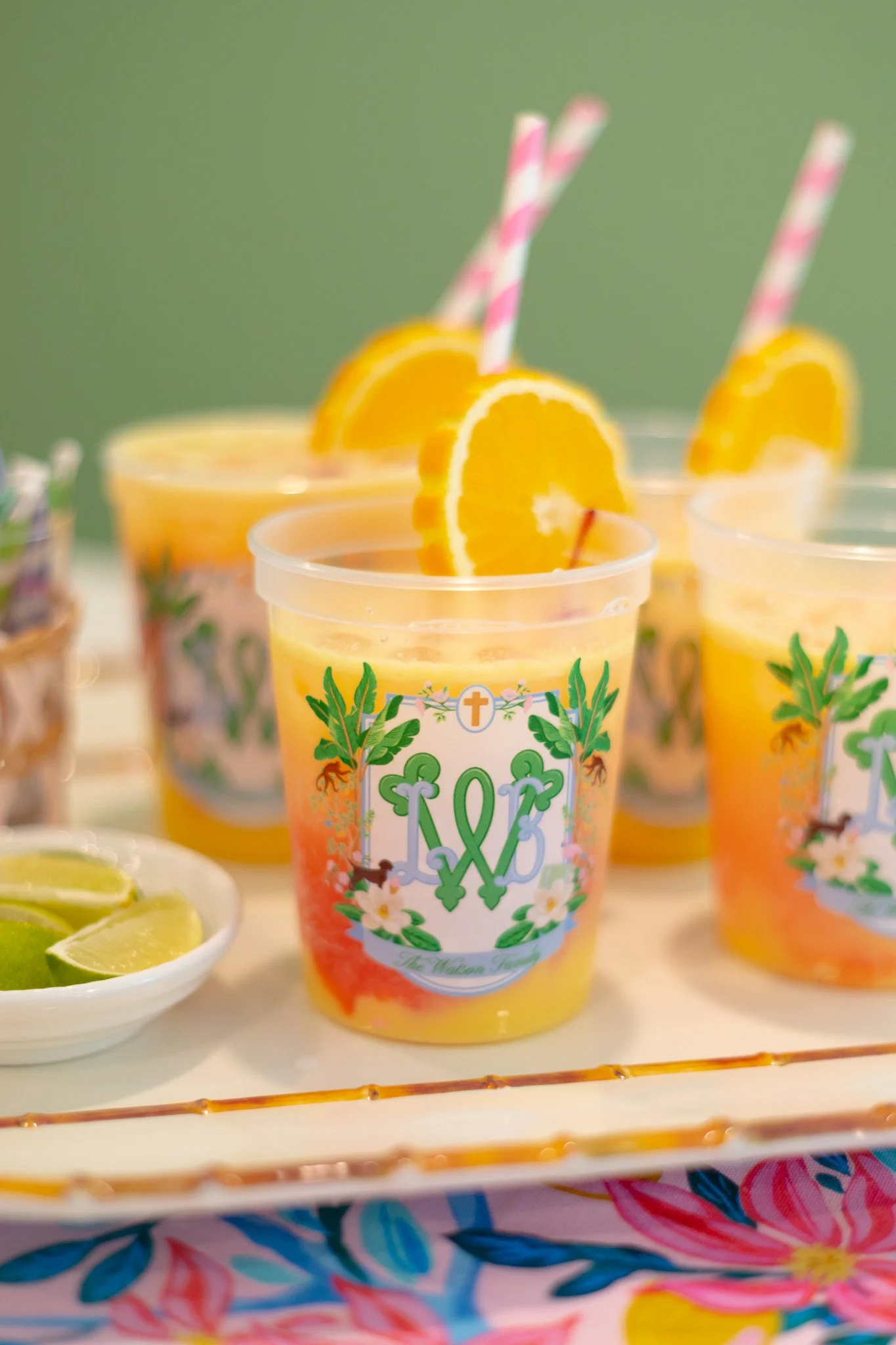 Three cups of lemonade garnished with orange slices and striped paper straws, placed on a tray with lime wedges nearby.