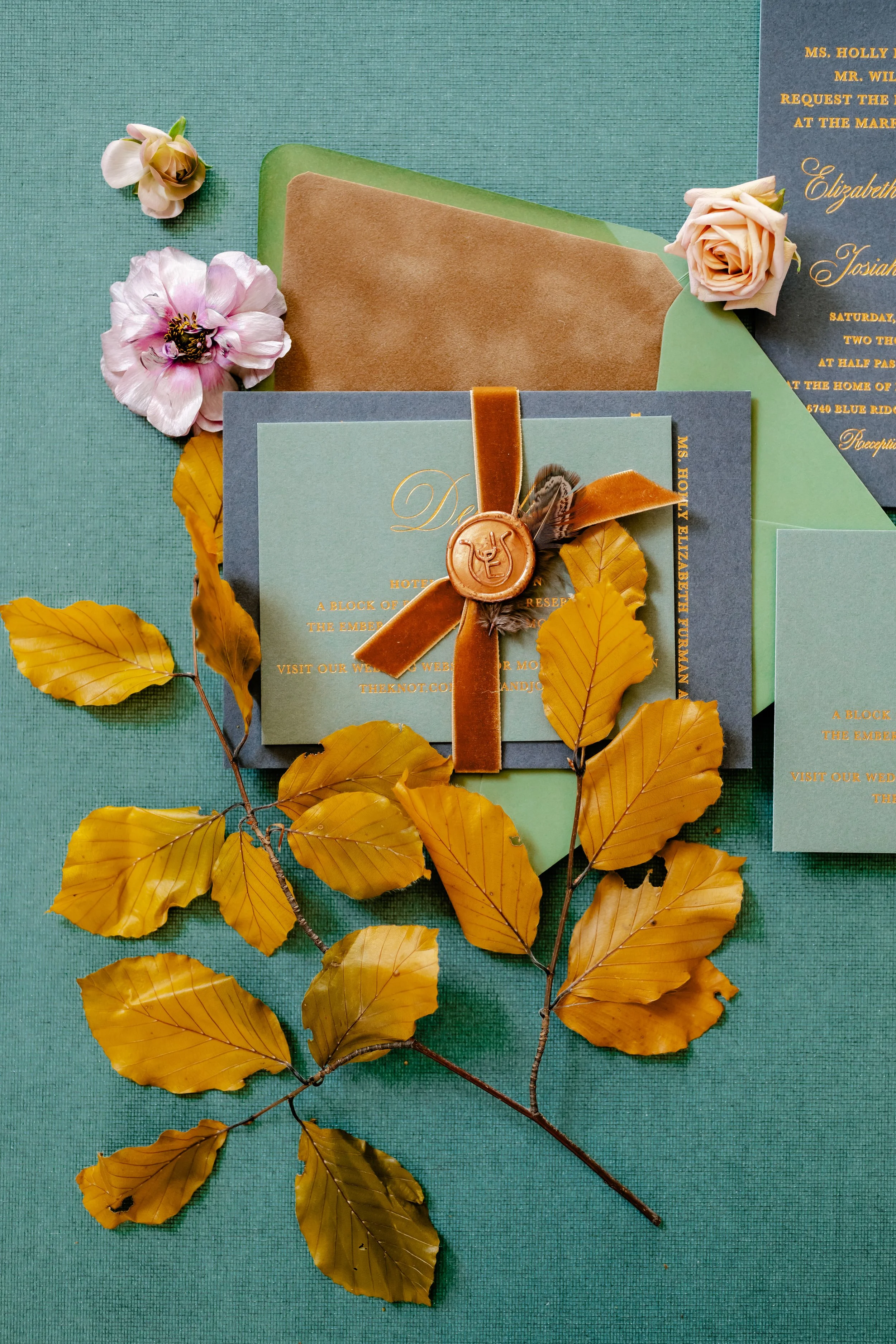 Wedding invitation suite with floral accents and autumn leaves on a teal background.