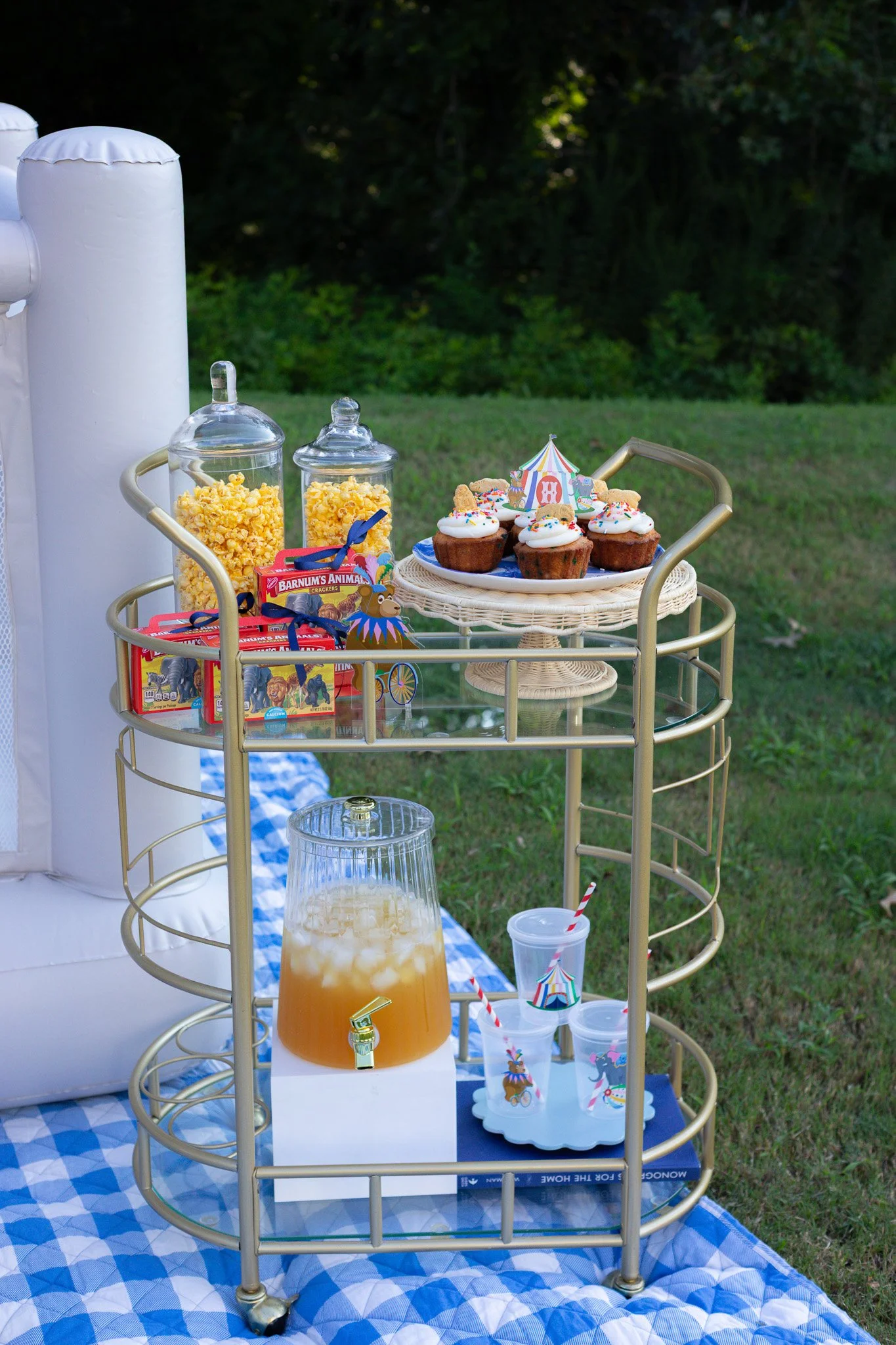 A dessert and snack cart with cupcakes, popcorn, and beverages at an outdoor party setup.
