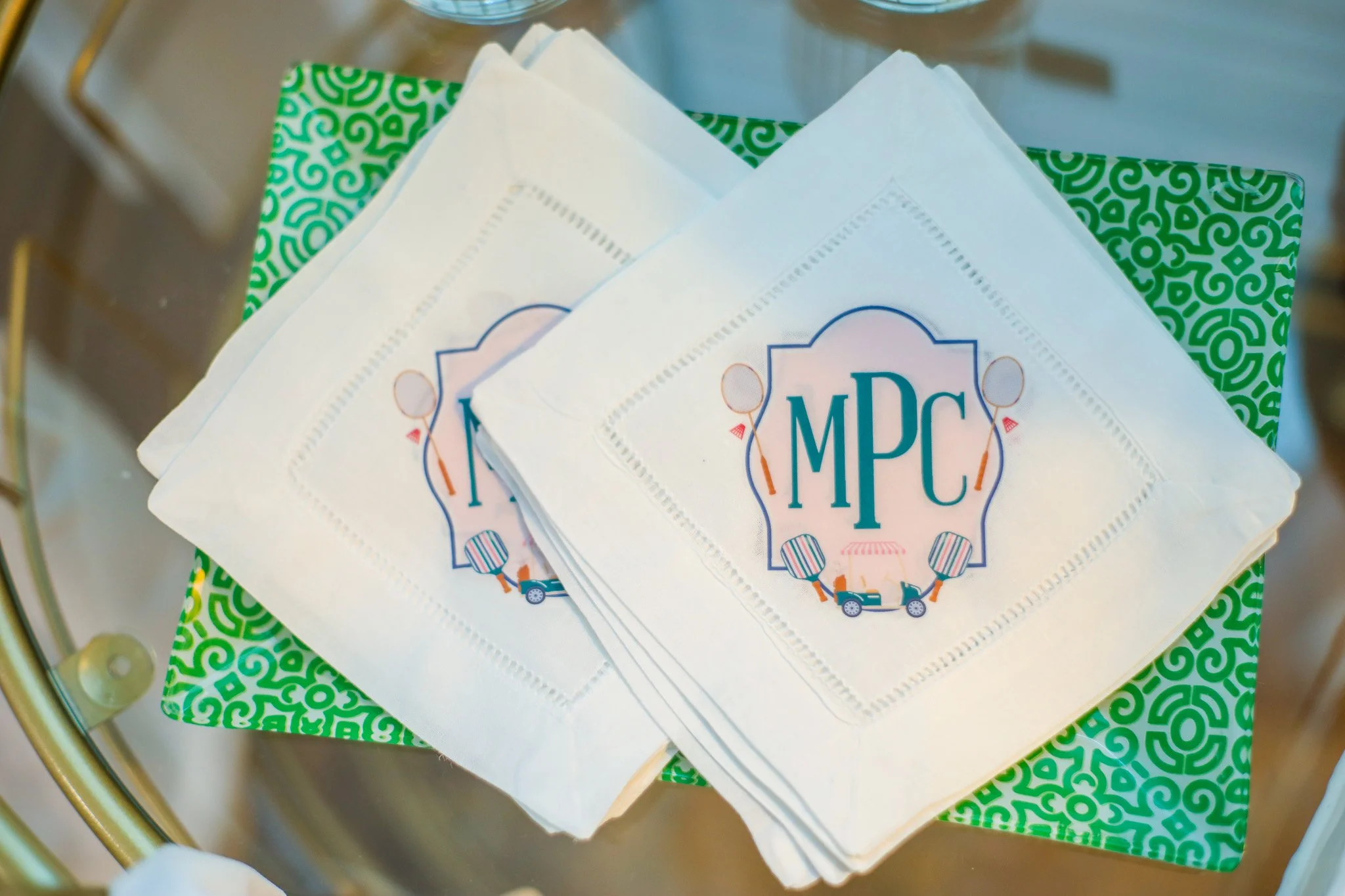 Stack of white paper napkins with the blue 'MPC' logo, placed on a green patterned napkin inside a metal shopping cart.