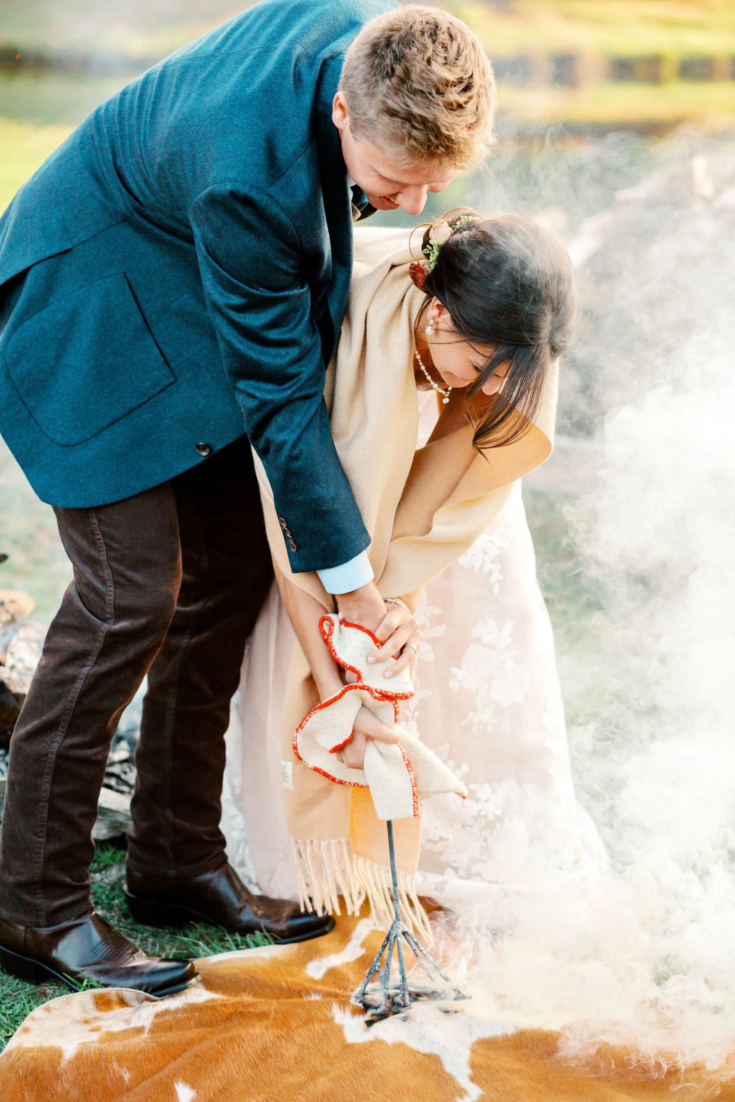 A couple in formal attire performing a traditional outdoor ceremony involving fire, on a cowhide rug.