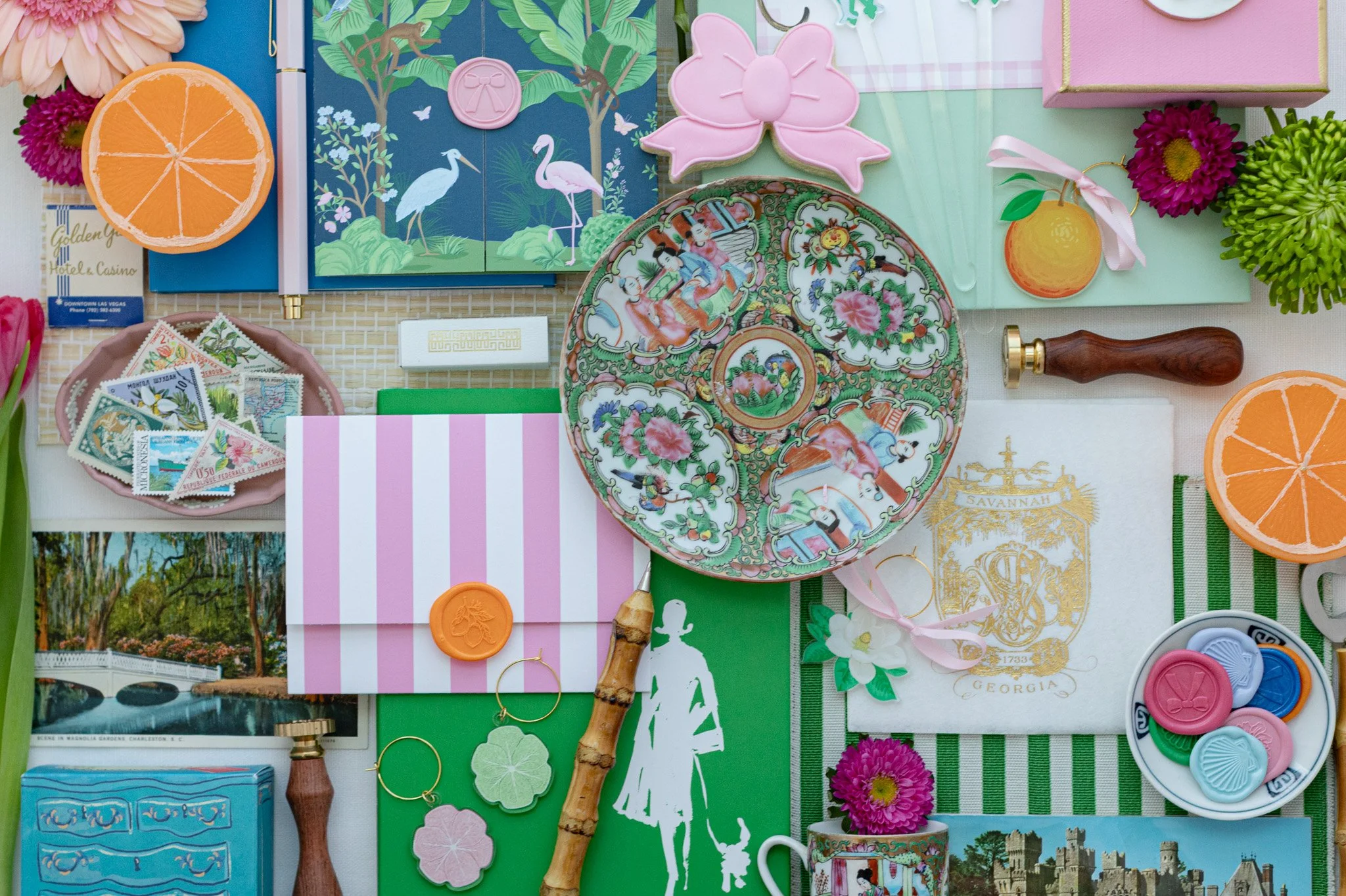 An assortment of colorful souvenirs and decorative items including ceramic plates with floral and animal motifs, paper flowers, postcards, stamps, a small blue dresser, jewelry, and stationery, arranged on a display board.