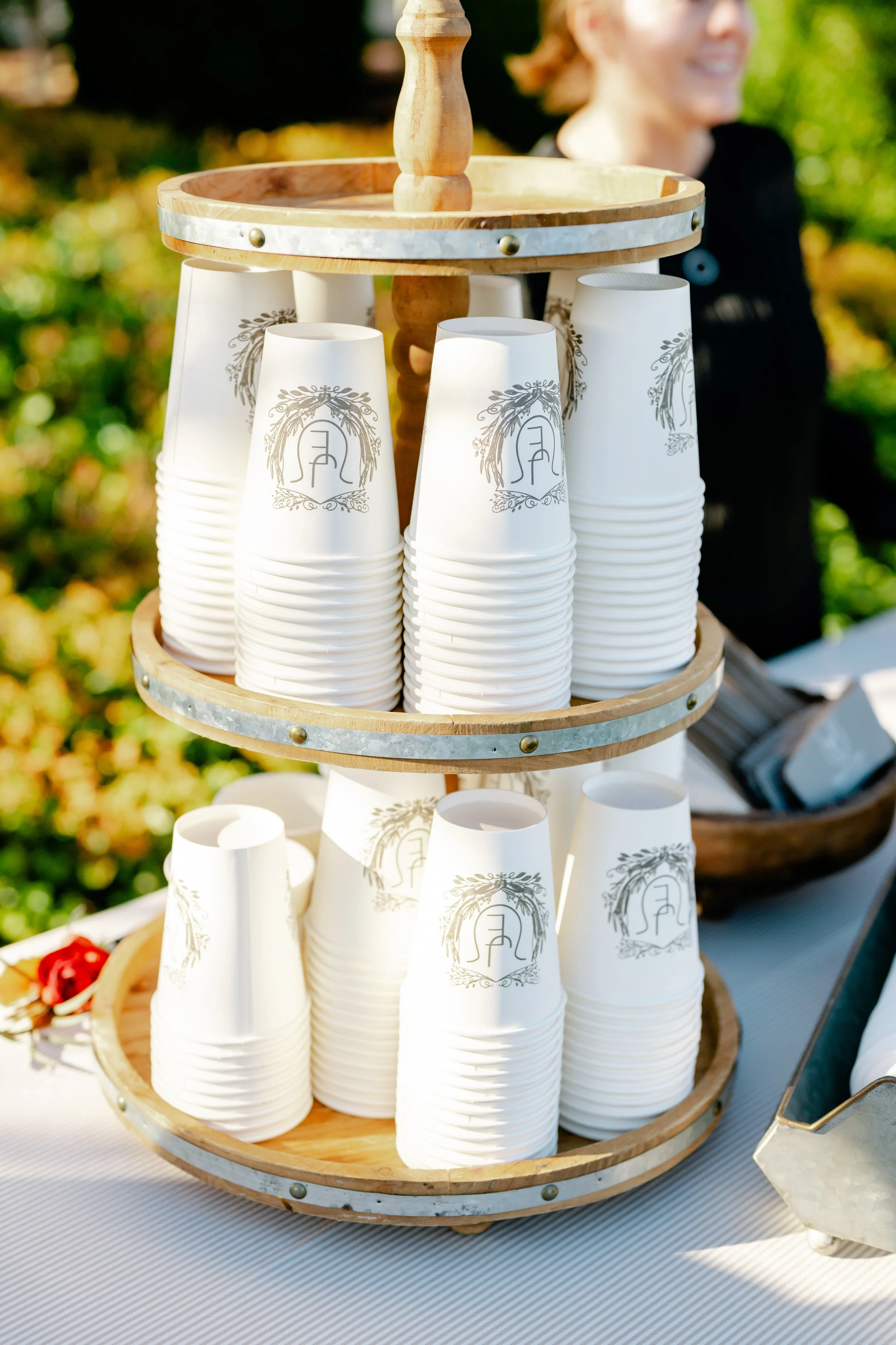 Stacked white paper cups with a logo, on wooden circular tiers, outdoors on a table.