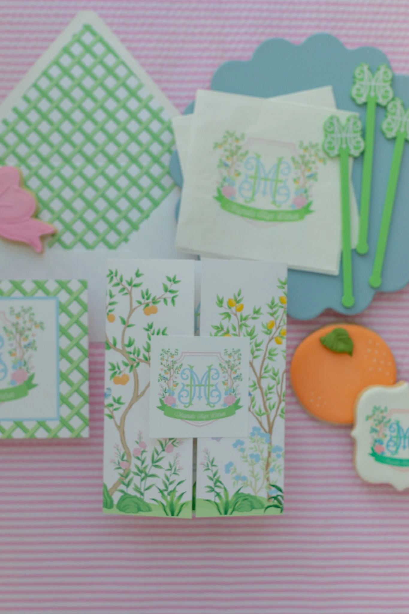 Decorative stationery and cookies with garden theme and monogrammed designs on pink striped background.