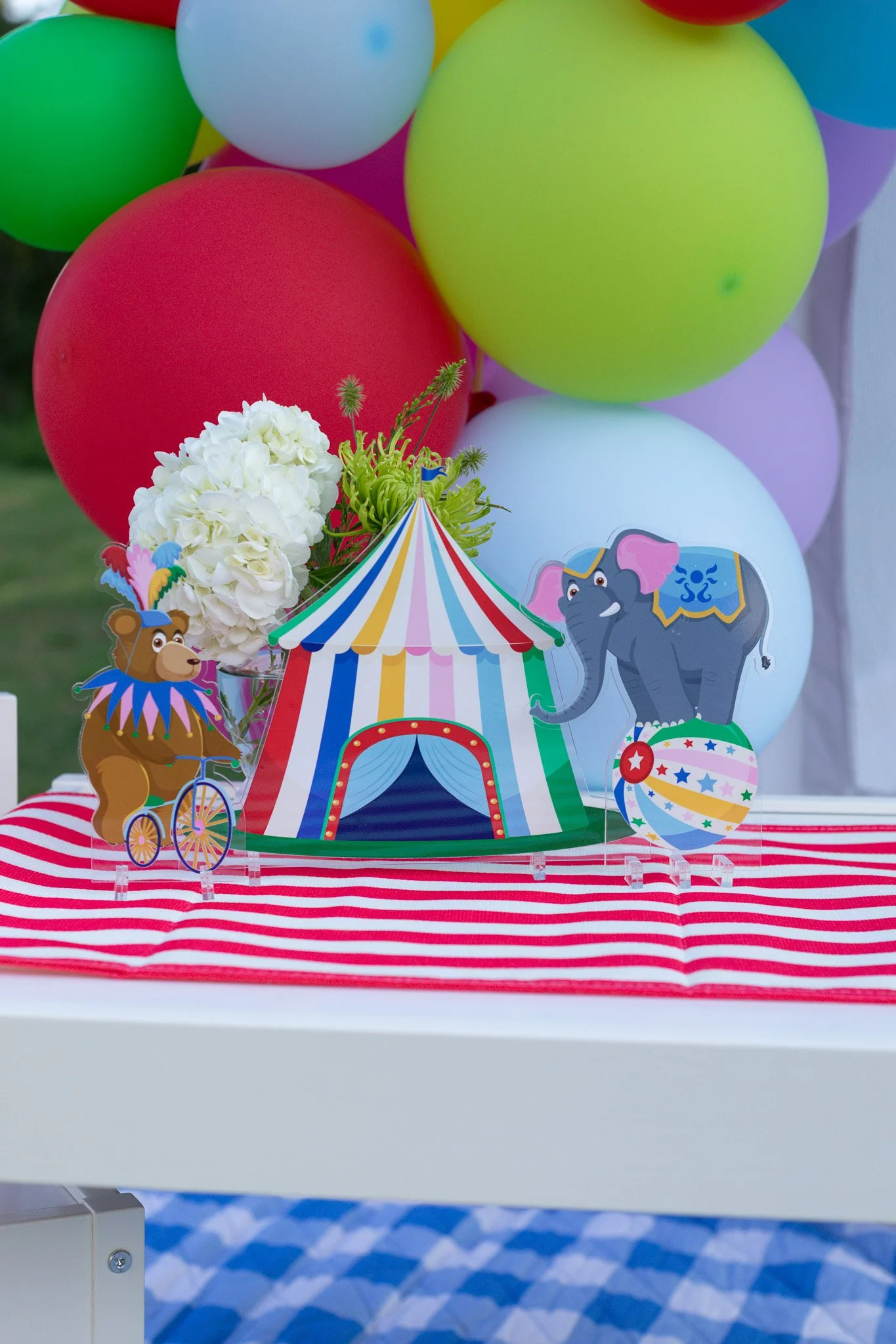 Circus-themed party setup with balloons, a striped tablecloth, a paper tent, and animal decorations including a bear on a unicycle and an elephant with a ball.
