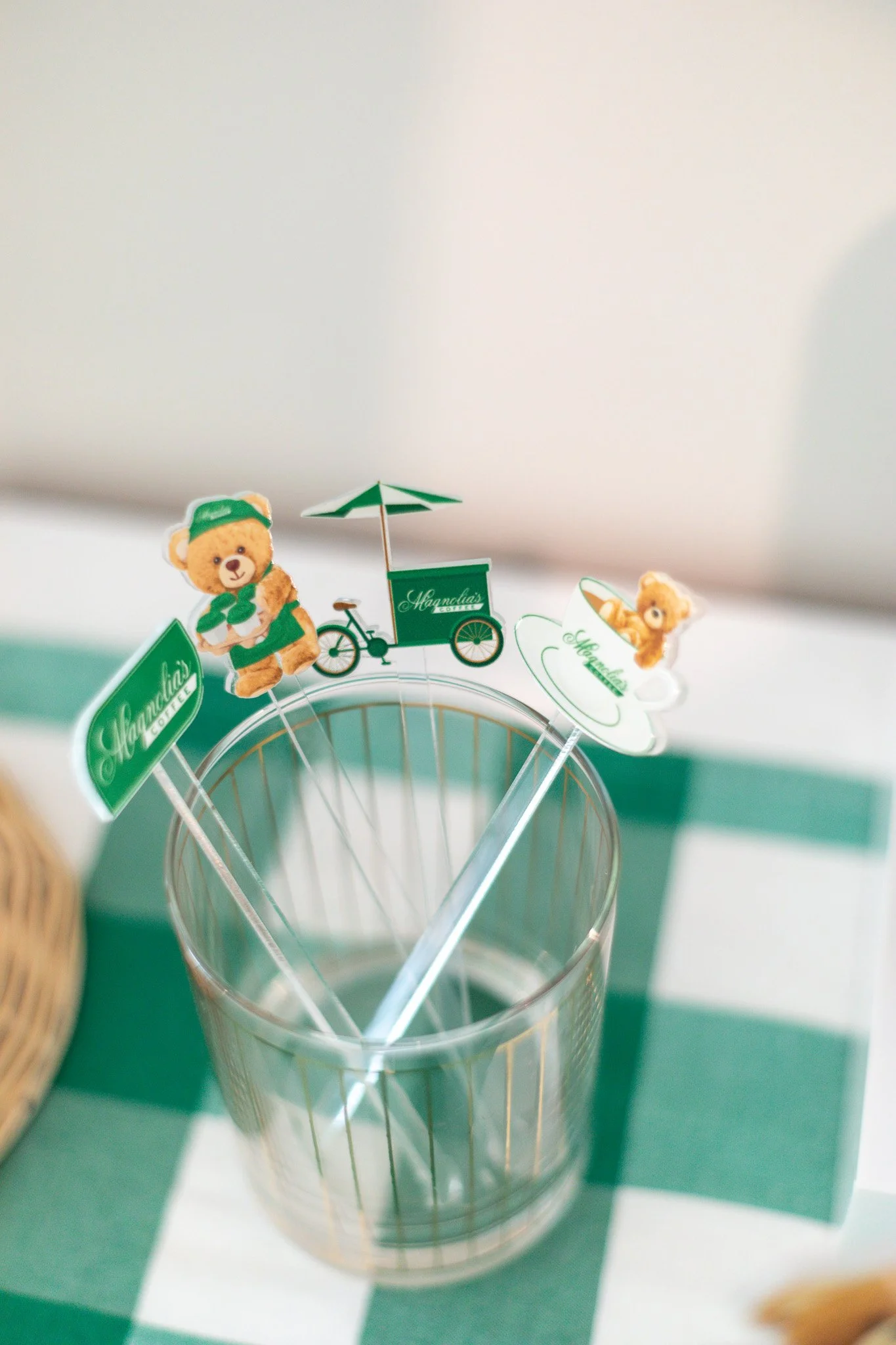 Decorative drink stirrers with teddy bear and café-themed designs in a glass