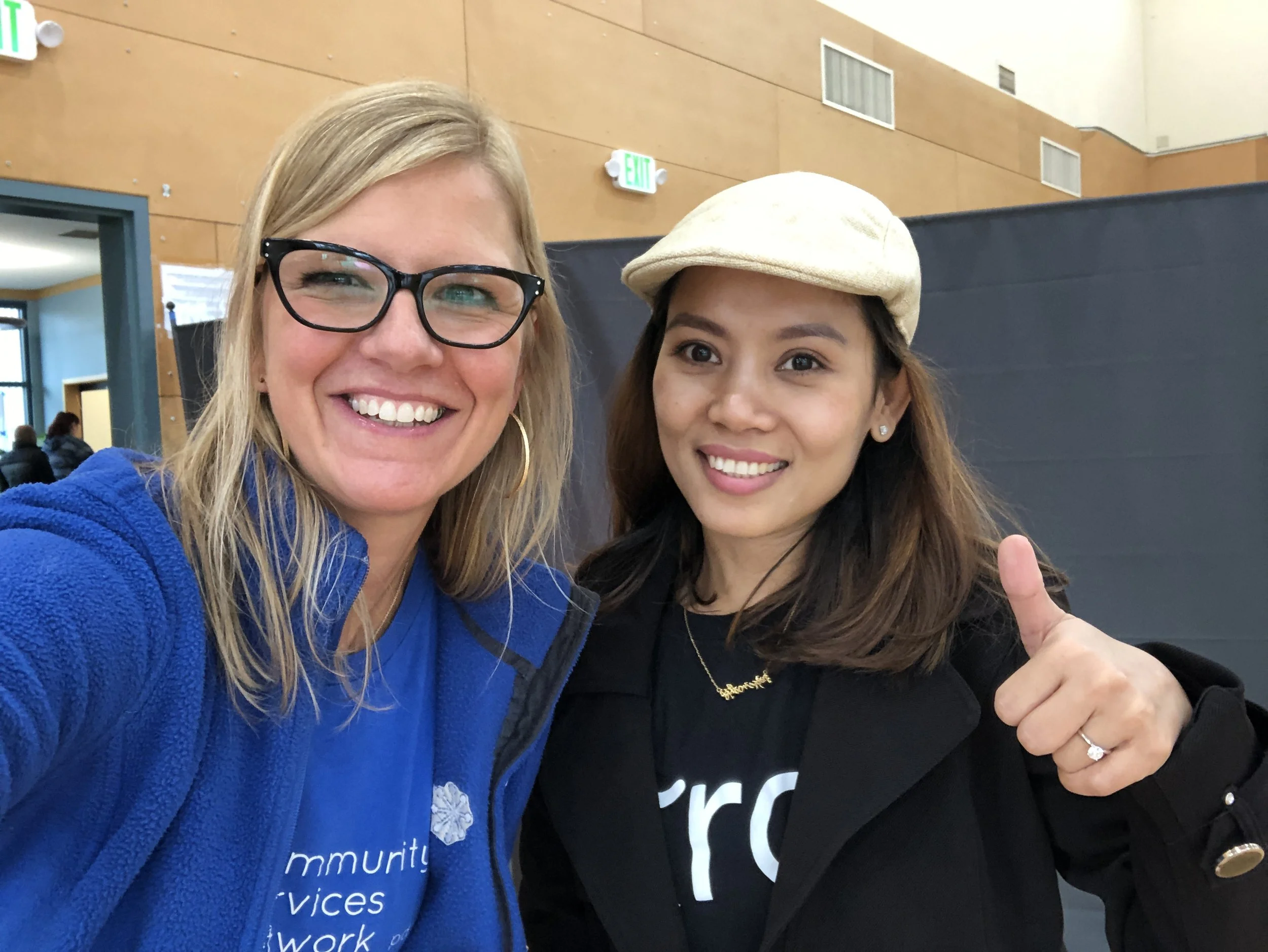  Two CSN staff members smiling together at an indoor community event, one wearing a Community Services Network sweatshirt. 