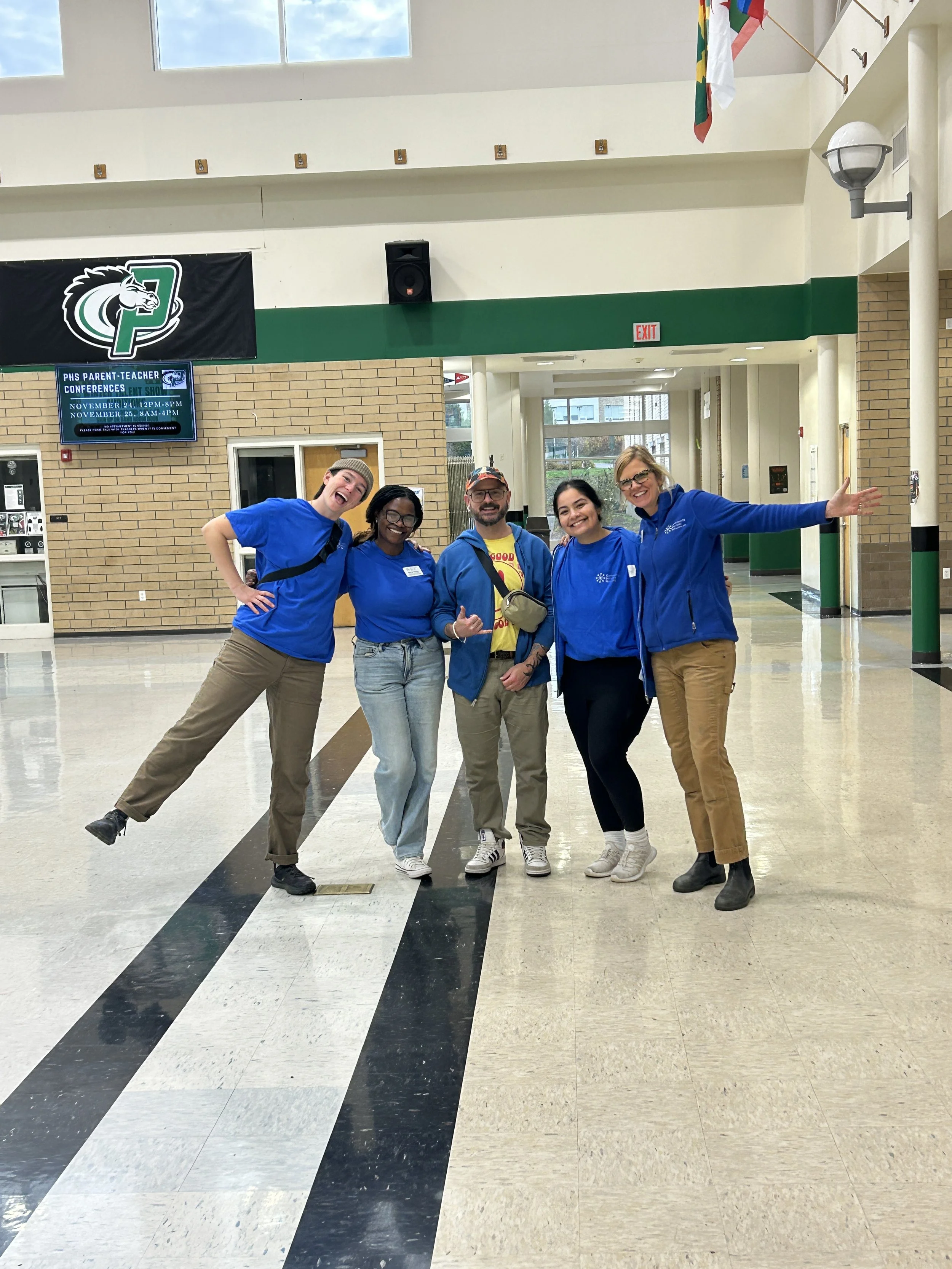  Four Community Services Network team members in blue sweatshirts posing together in a school hallway at a CSN community resource fair. 
