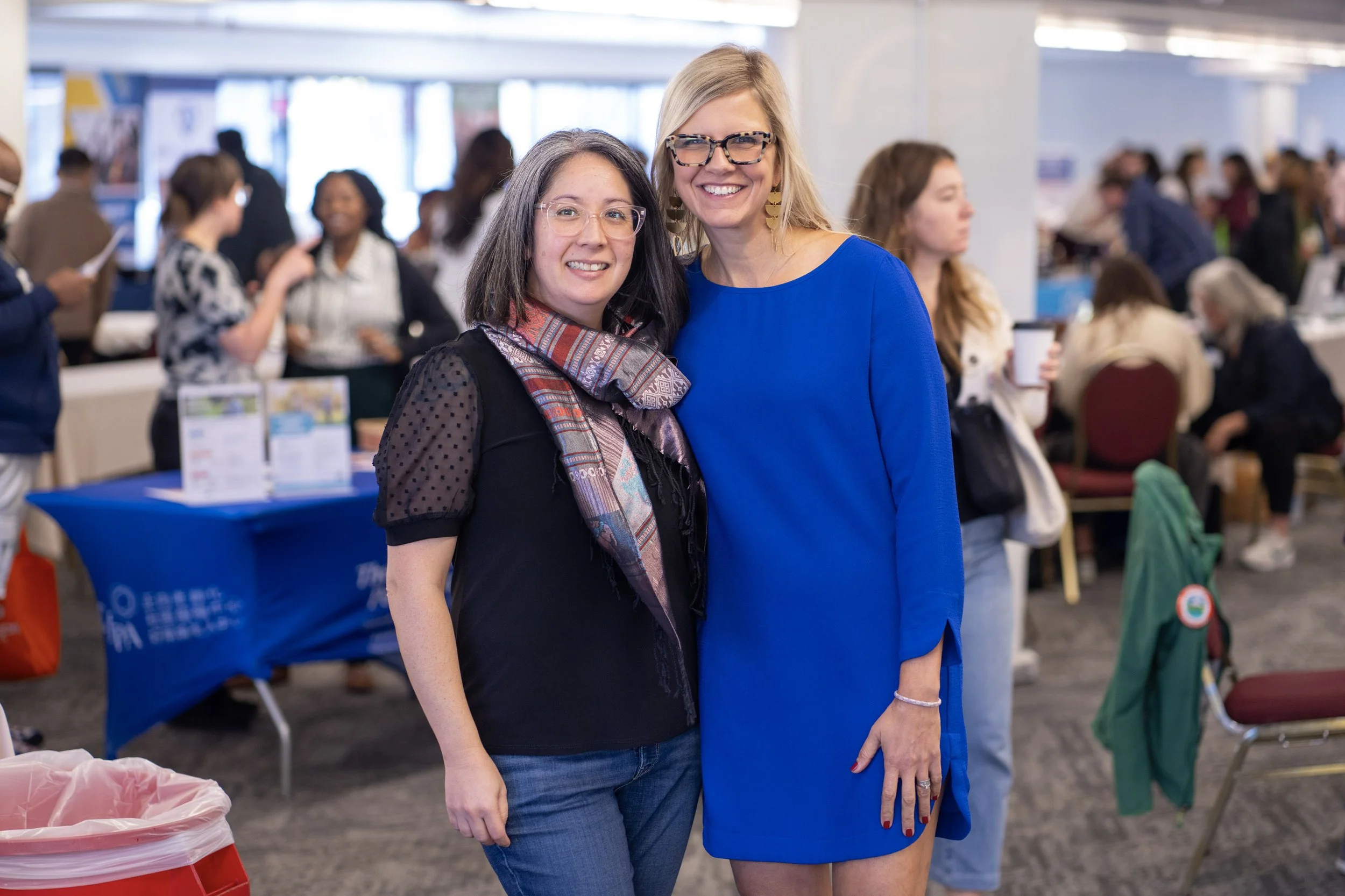  Two women smiling together at an indoor CSN Nonprofit Connect event, with vendor and resource tables visible in the background in Portland, Oregon. 