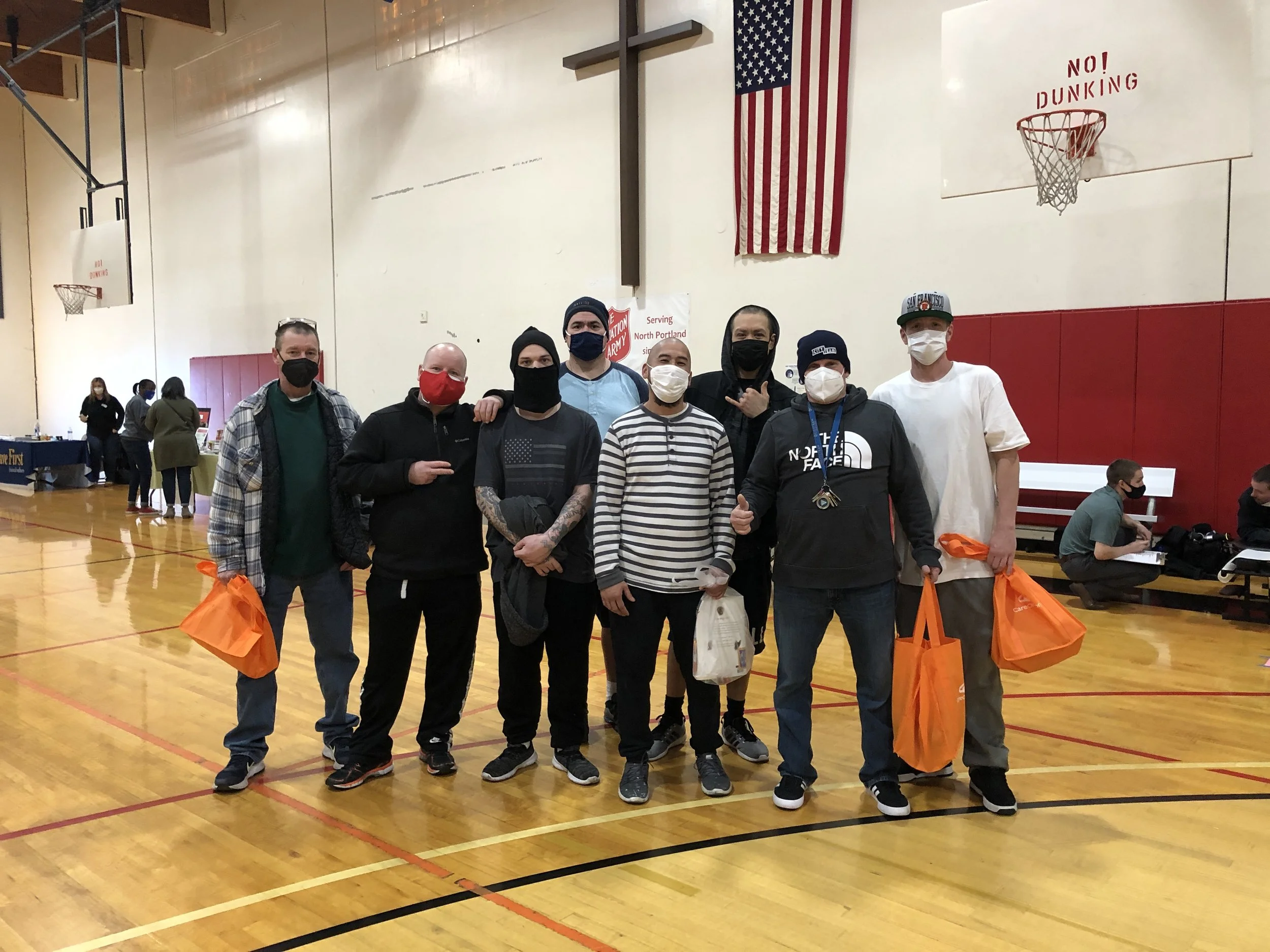  A group of community members wearing masks and holding orange tote bags at a Salvation Army gymnasium during a CSN community resource fair in North Portland, Oregon. 