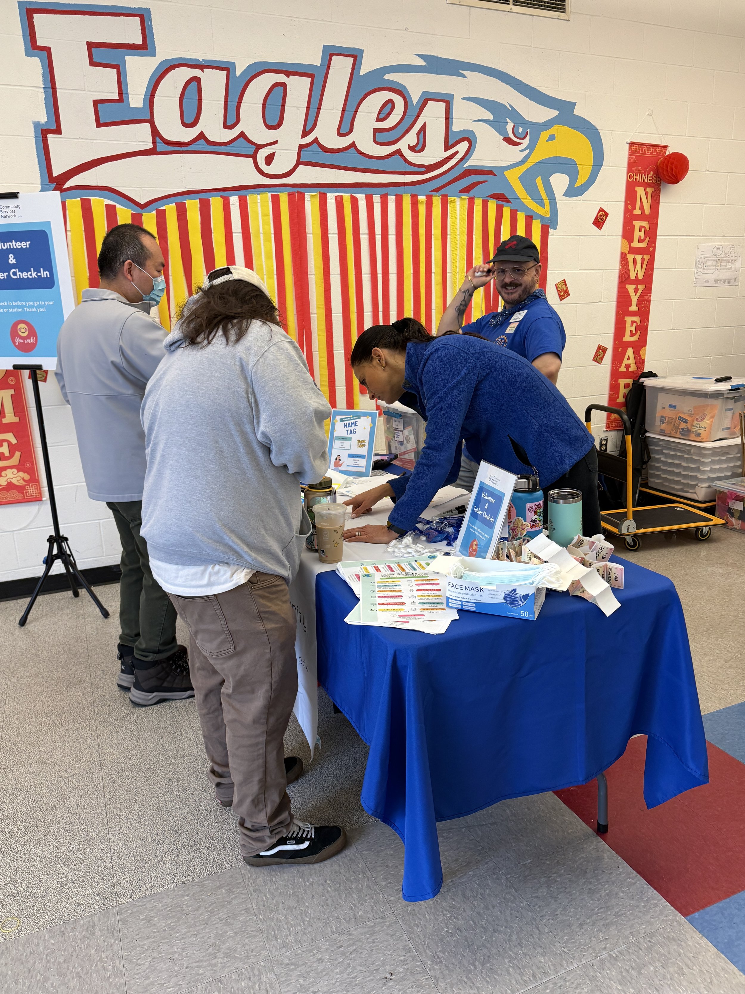  CSN volunteers staffing an information booth inside a school gymnasium decorated with an Eagles mural at a CSN community resource fair in Portland, Oregon. 