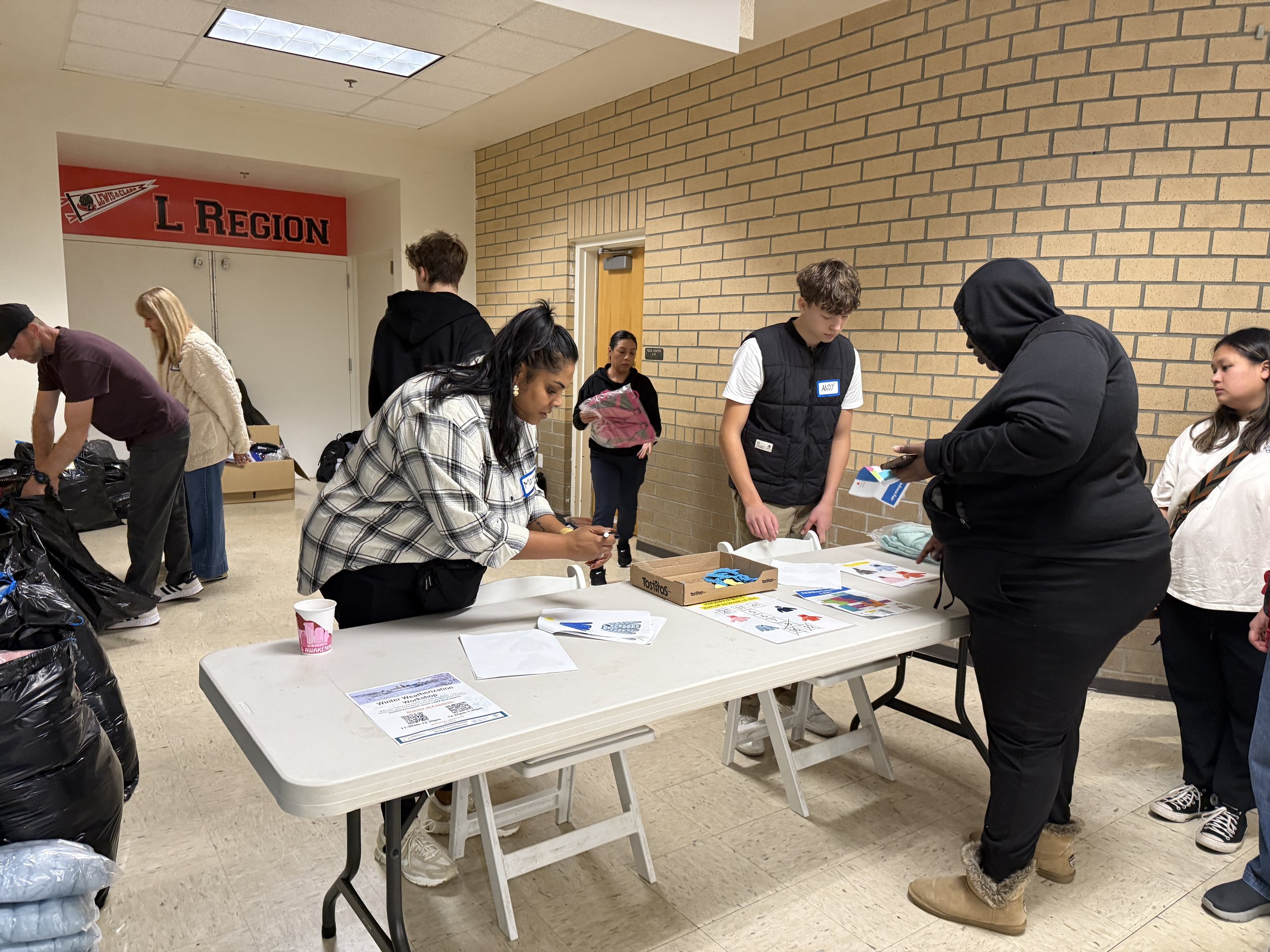 CSN volunteers and participants sorting donated clothing and resource materials at tables inside a school hallway during a community resource event in Portland, Oregon. 