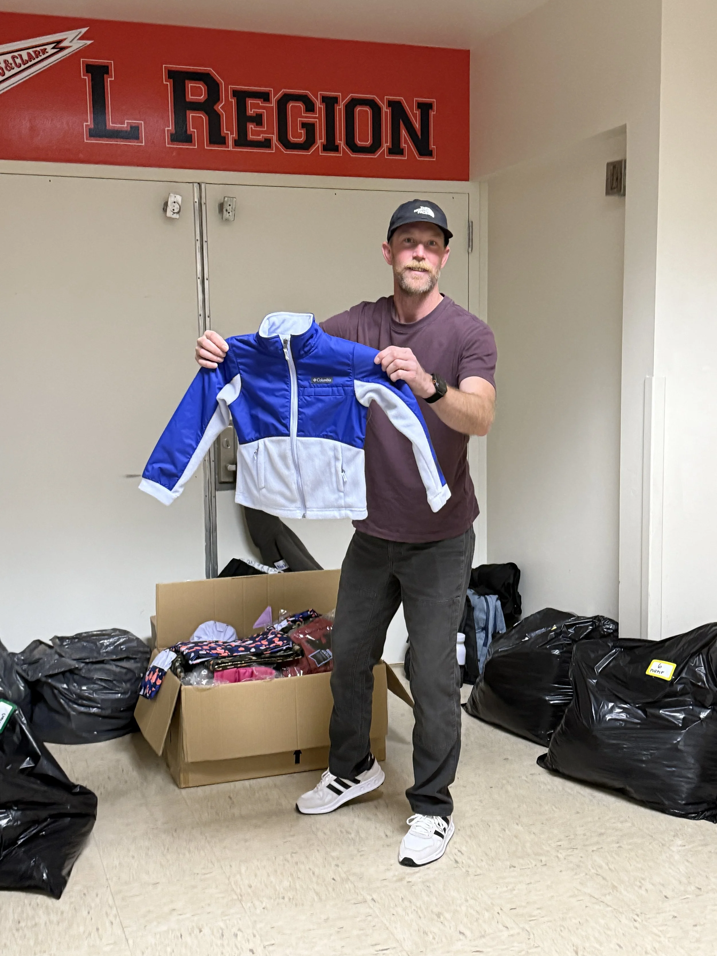  A CSN volunteer holding up a donated children's jacket next to boxes of supplies at a community clothing drive and resource fair event in Portland, Oregon. 