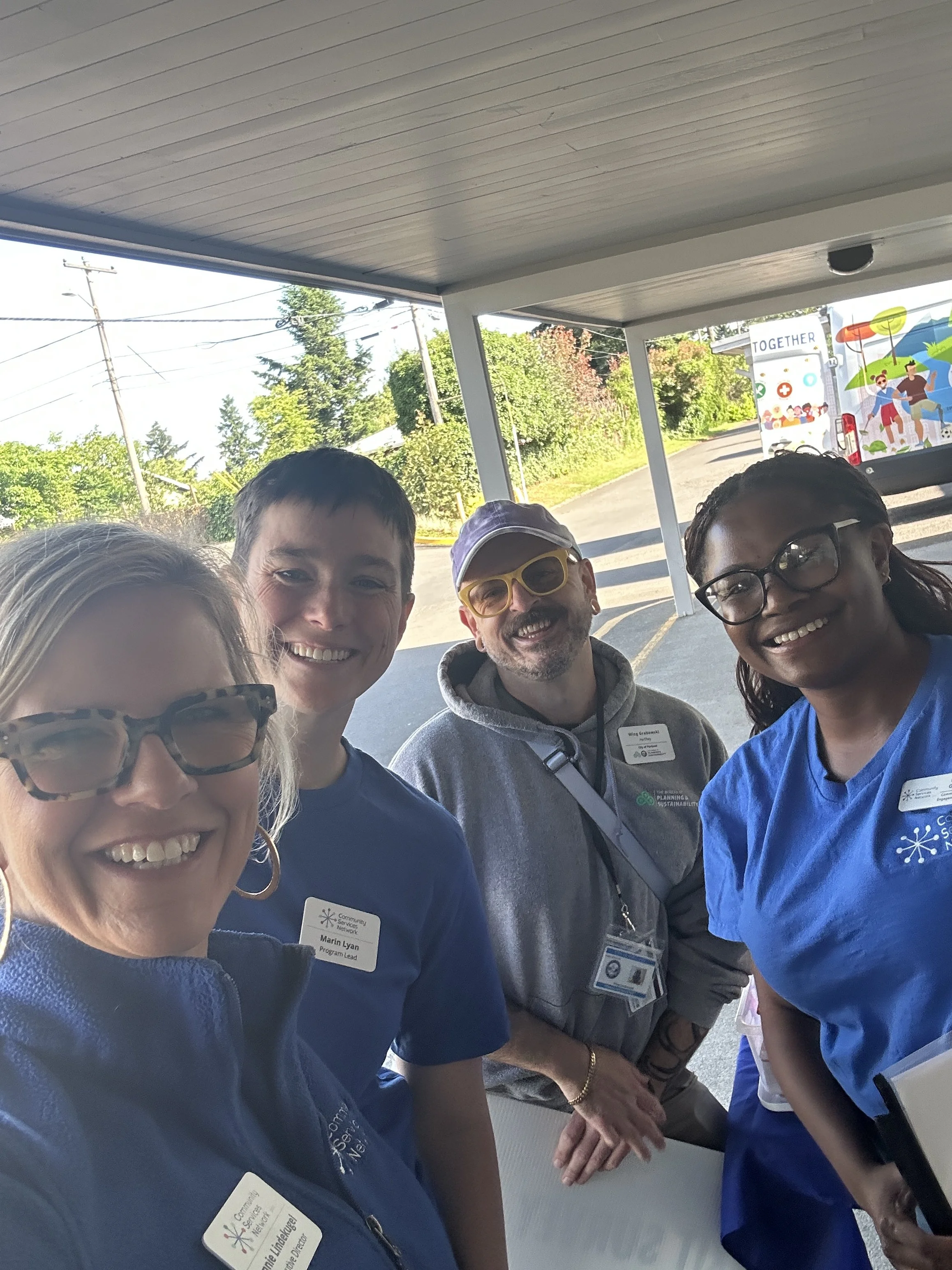  Four Community Services Network staff members and sponsors smiling together at an outdoor CSN community resource fair in Portland, Oregon. 