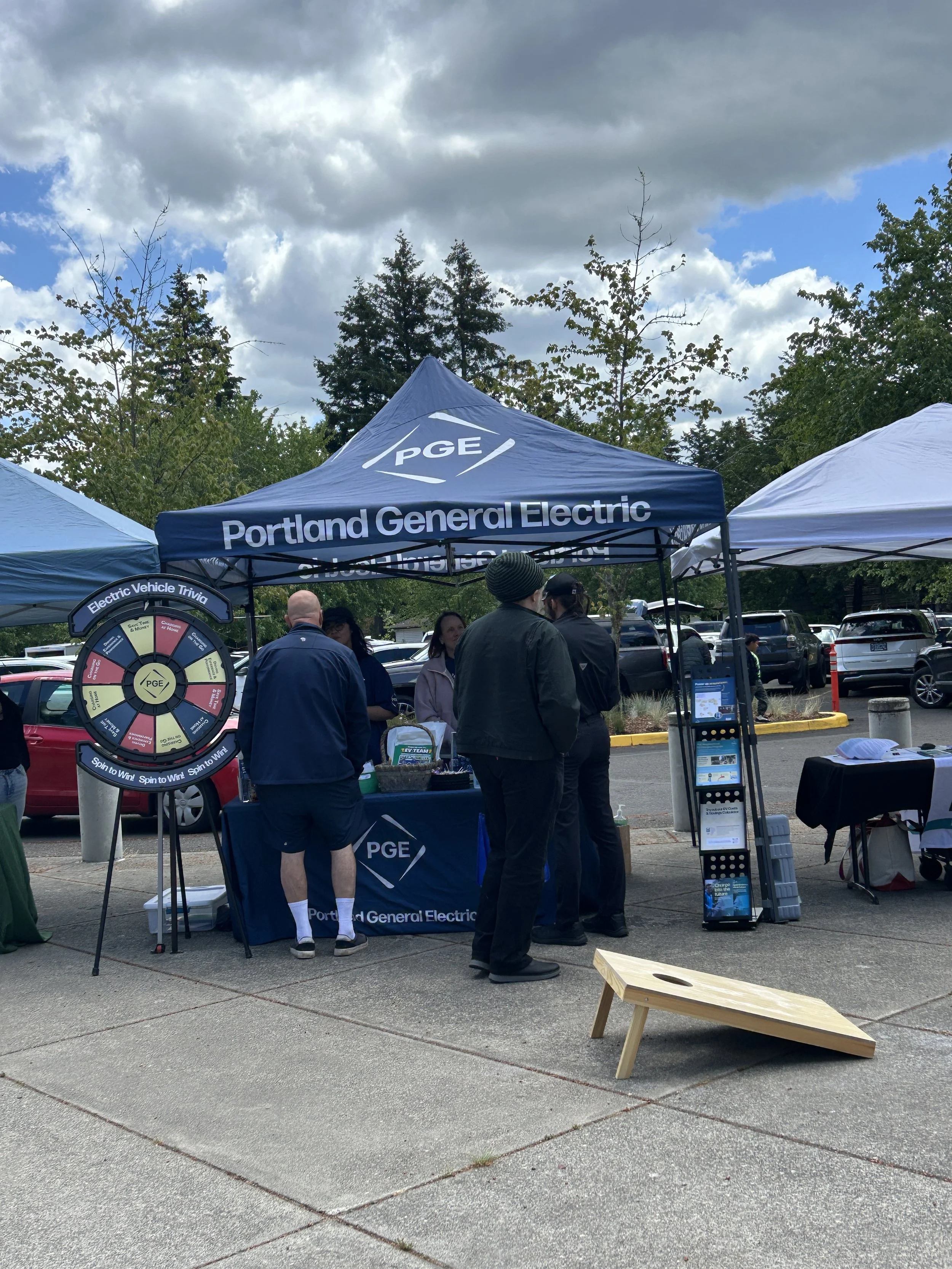  Portland General Electric sponsor booth with branded canopy tent and prize wheel at an outdoor CSN community resource fair in Portland, Oregon. 