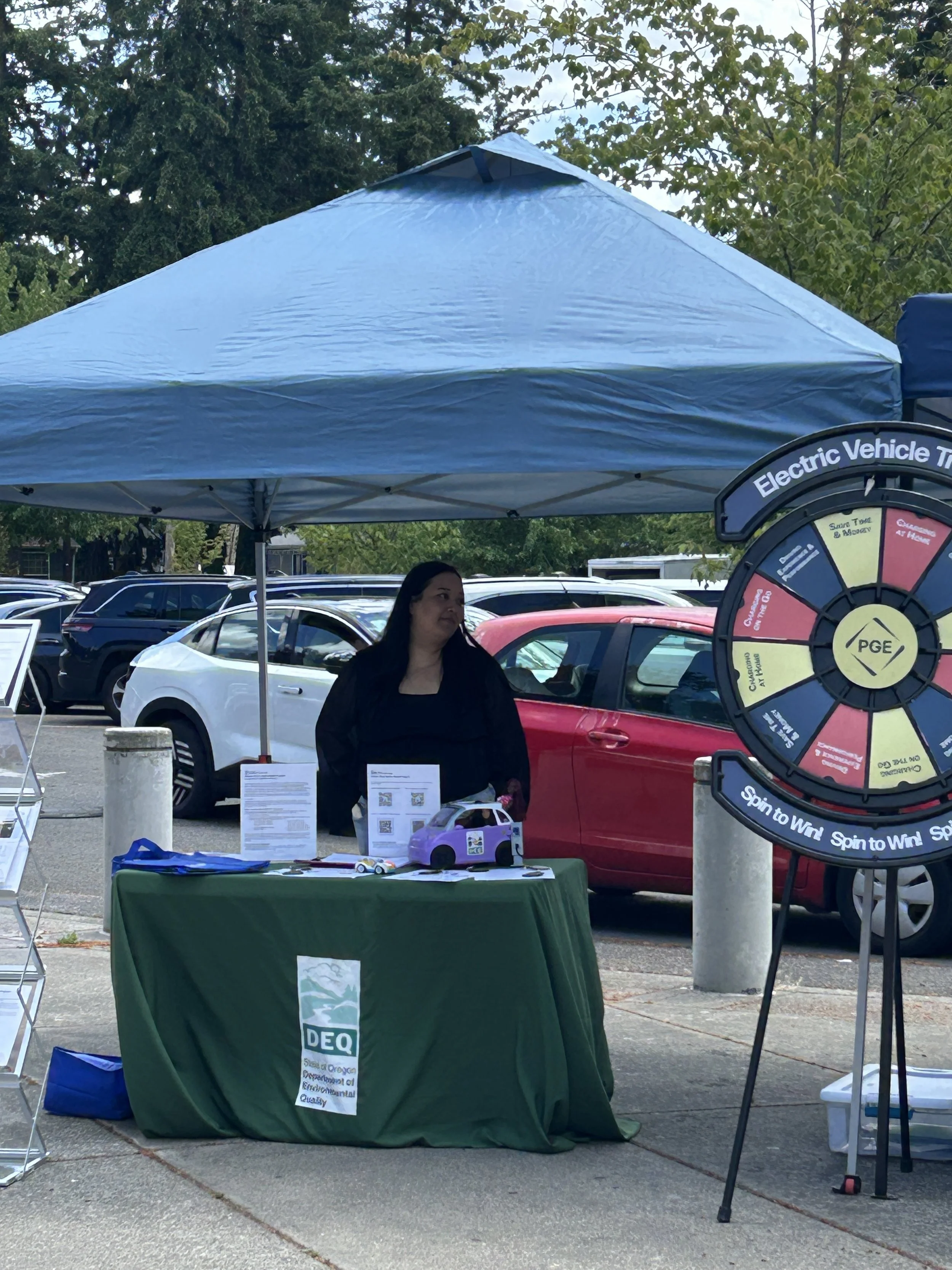 Outdoor sponsor booths featuring a Portland General Electric electric vehicle trivia wheel and an Oregon DEQ display at a CSN community resource fair. 