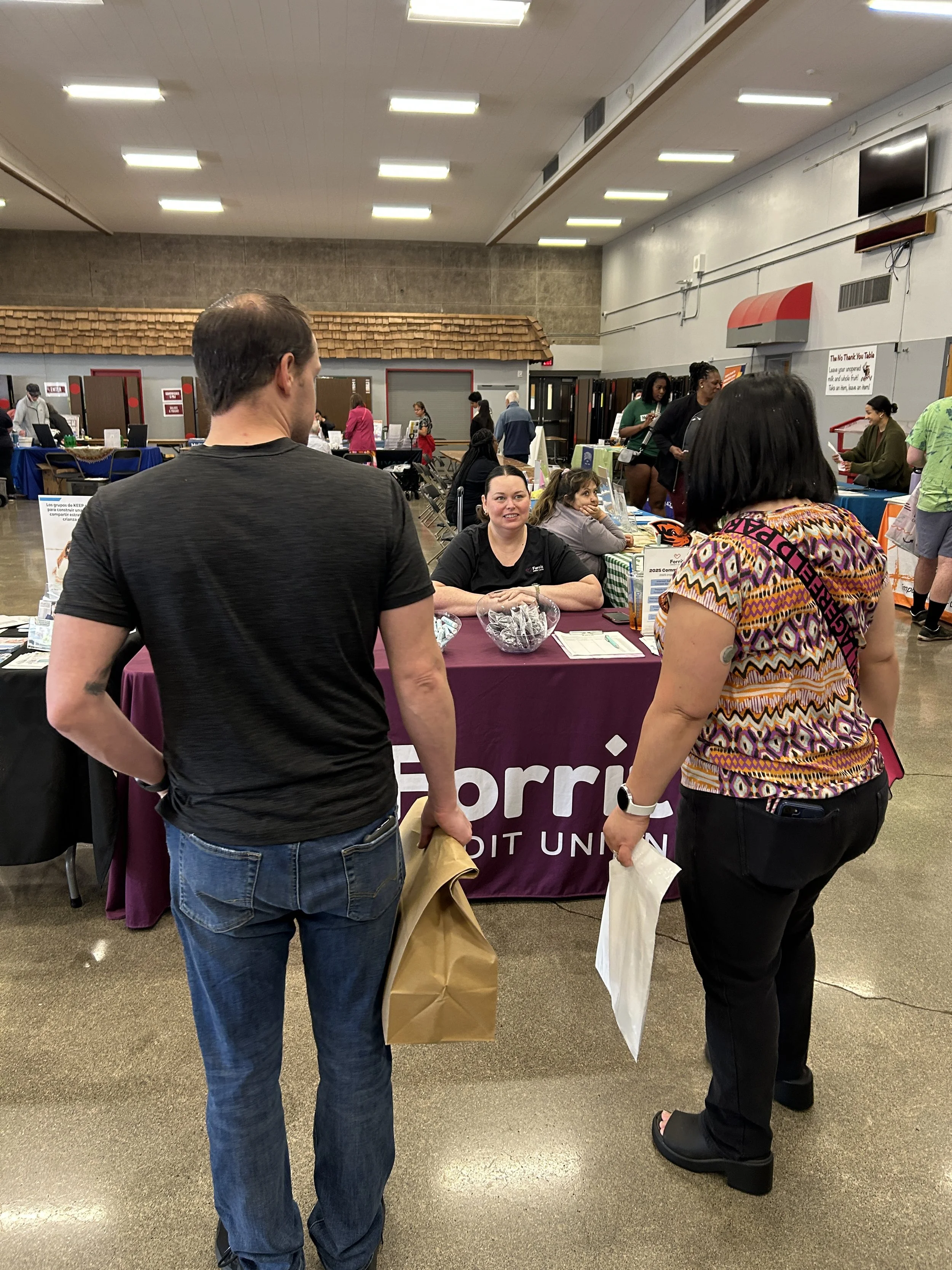  A community member speaking with a Forrit Credit Union sponsor representative at an indoor CSN community resource fair in Portland, Oregon. 