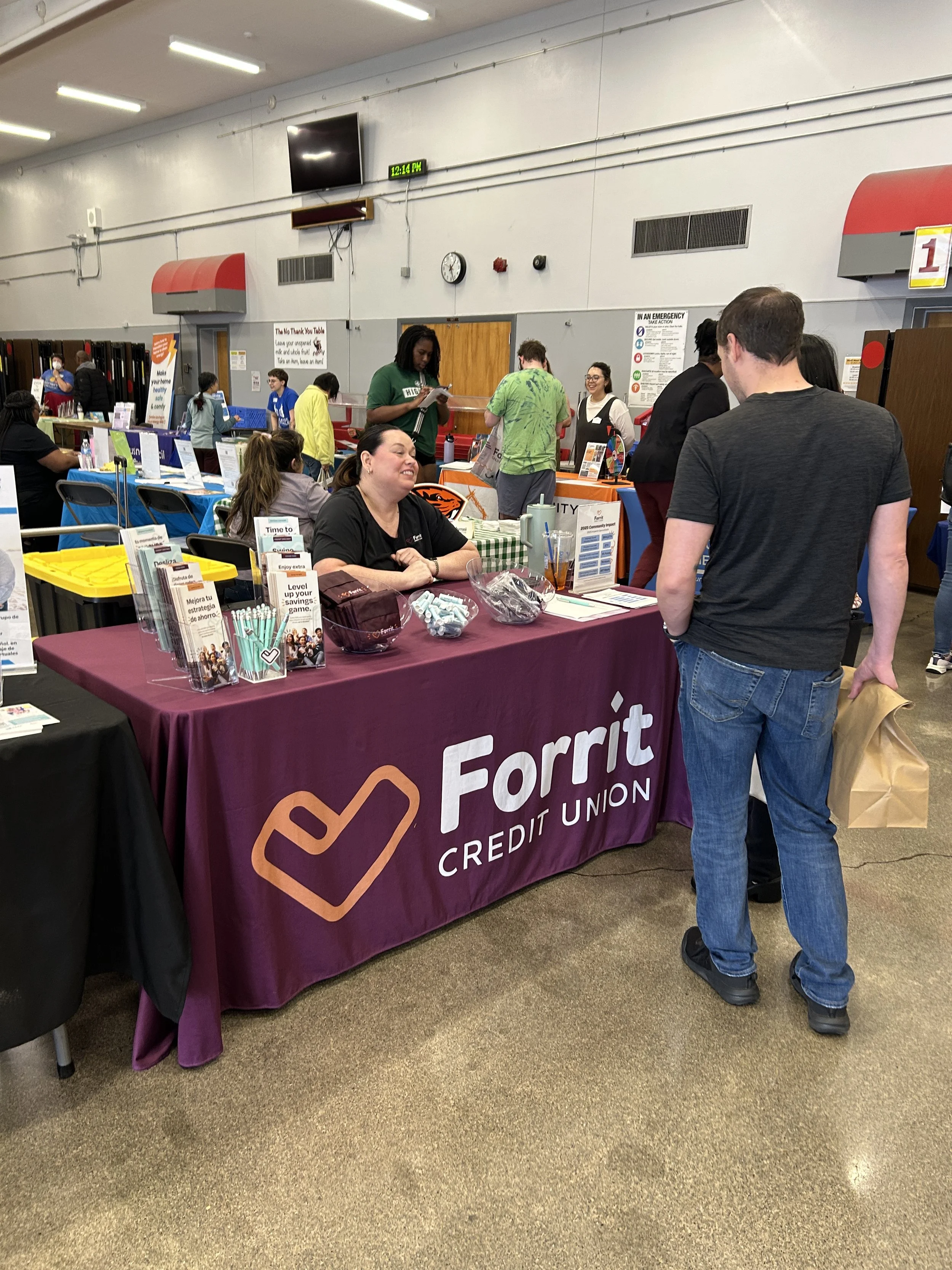  Forrit Credit Union sponsor table staffed by a representative at an indoor CSN community resource fair in Portland, Oregon. 