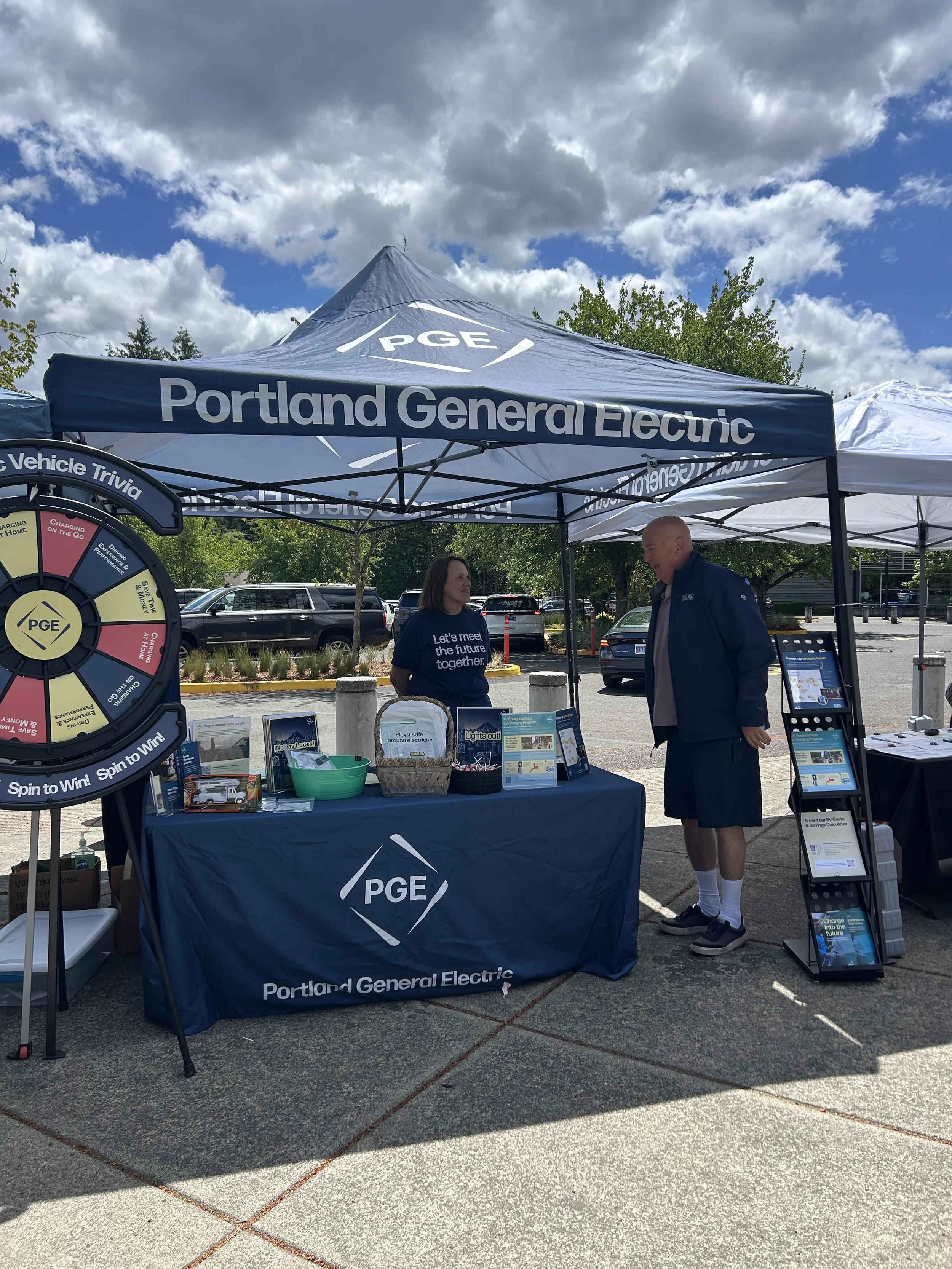 Portland General Electric outdoor sponsor booth with branded tent and electric vehicle trivia wheel at a CSN community resource fair in Portland, Oregon. 