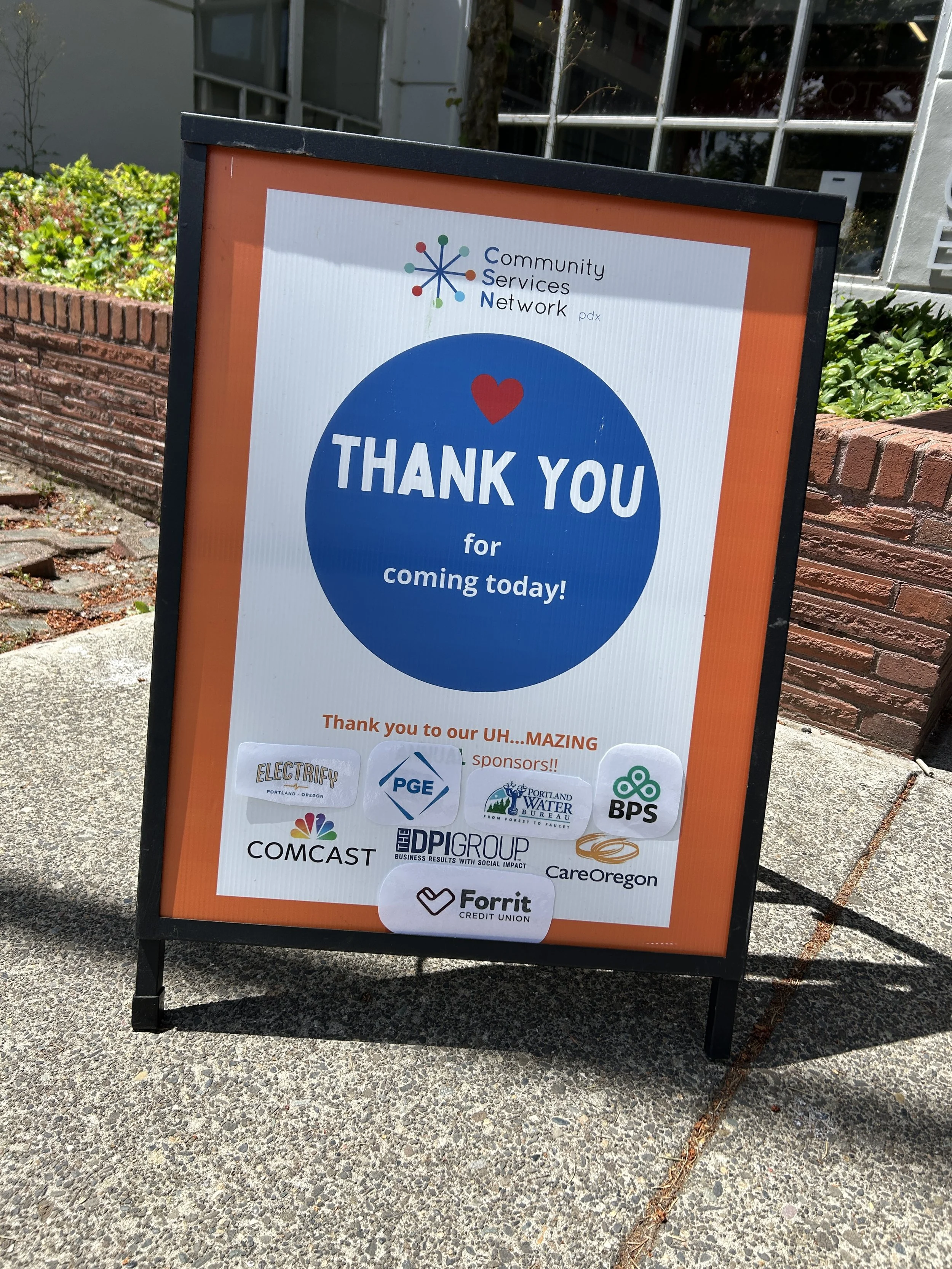  A Community Services Network sandwich board sign thanking event sponsors including PGE, DPI Group, CareOregon, BPS, Forrit Credit Union, and Comcast at a CSN event in Portland, Oregon. 