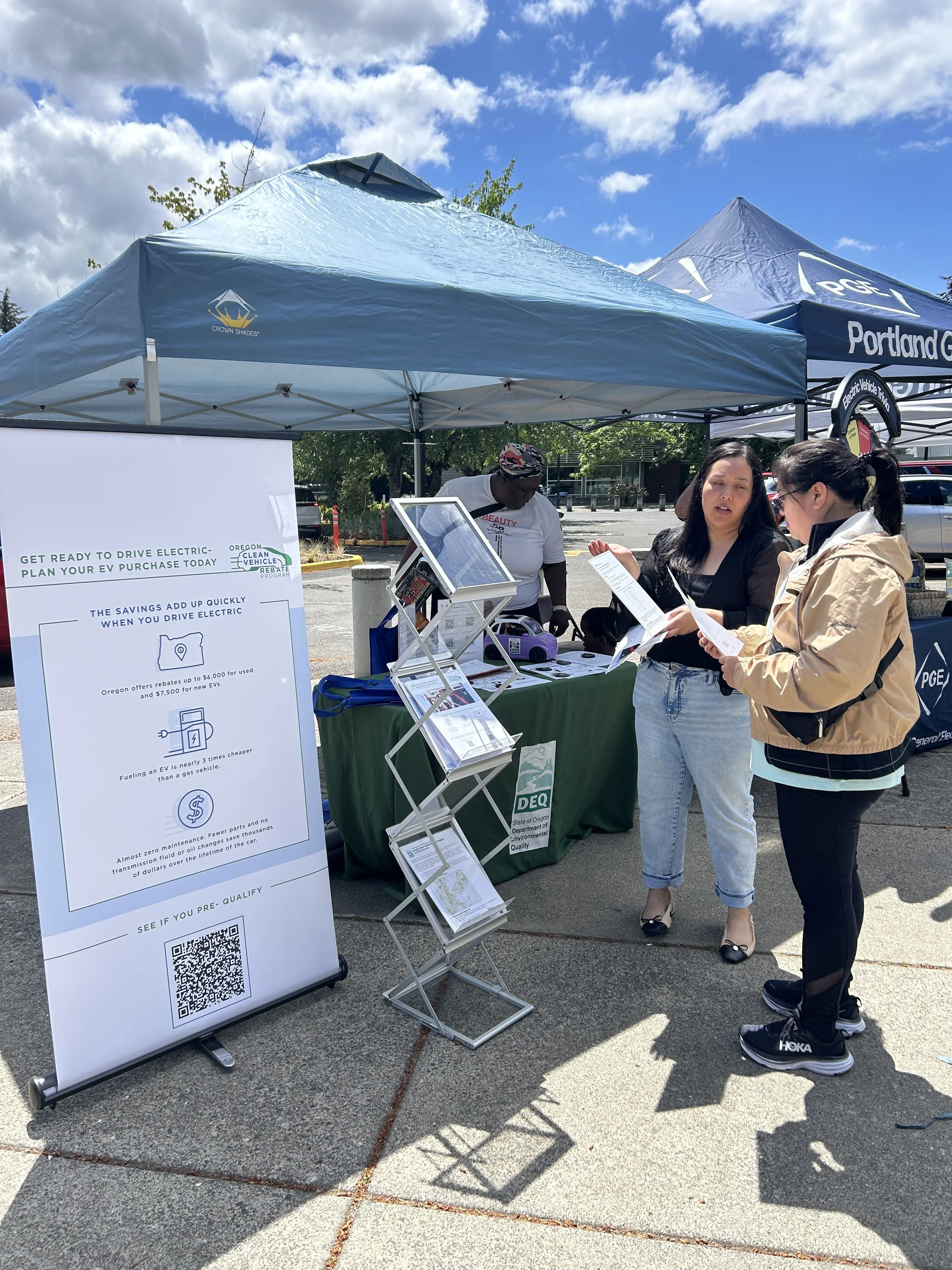  A community member reviewing electric vehicle information at an outdoor Portland General Electric sponsor booth during a CSN community resource fair. 