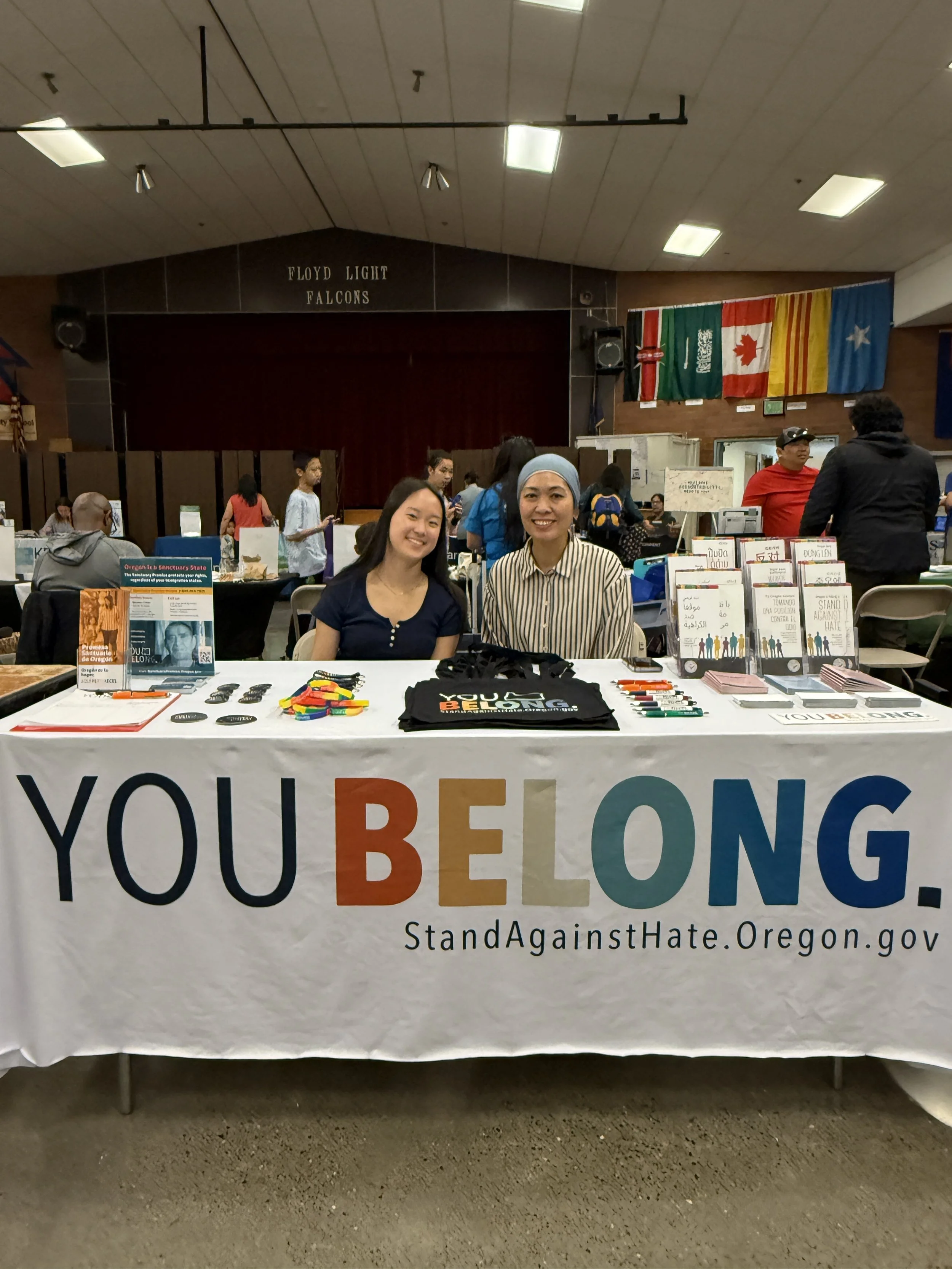 Two women at table at community event with tablecloth that reads, "You belong"
