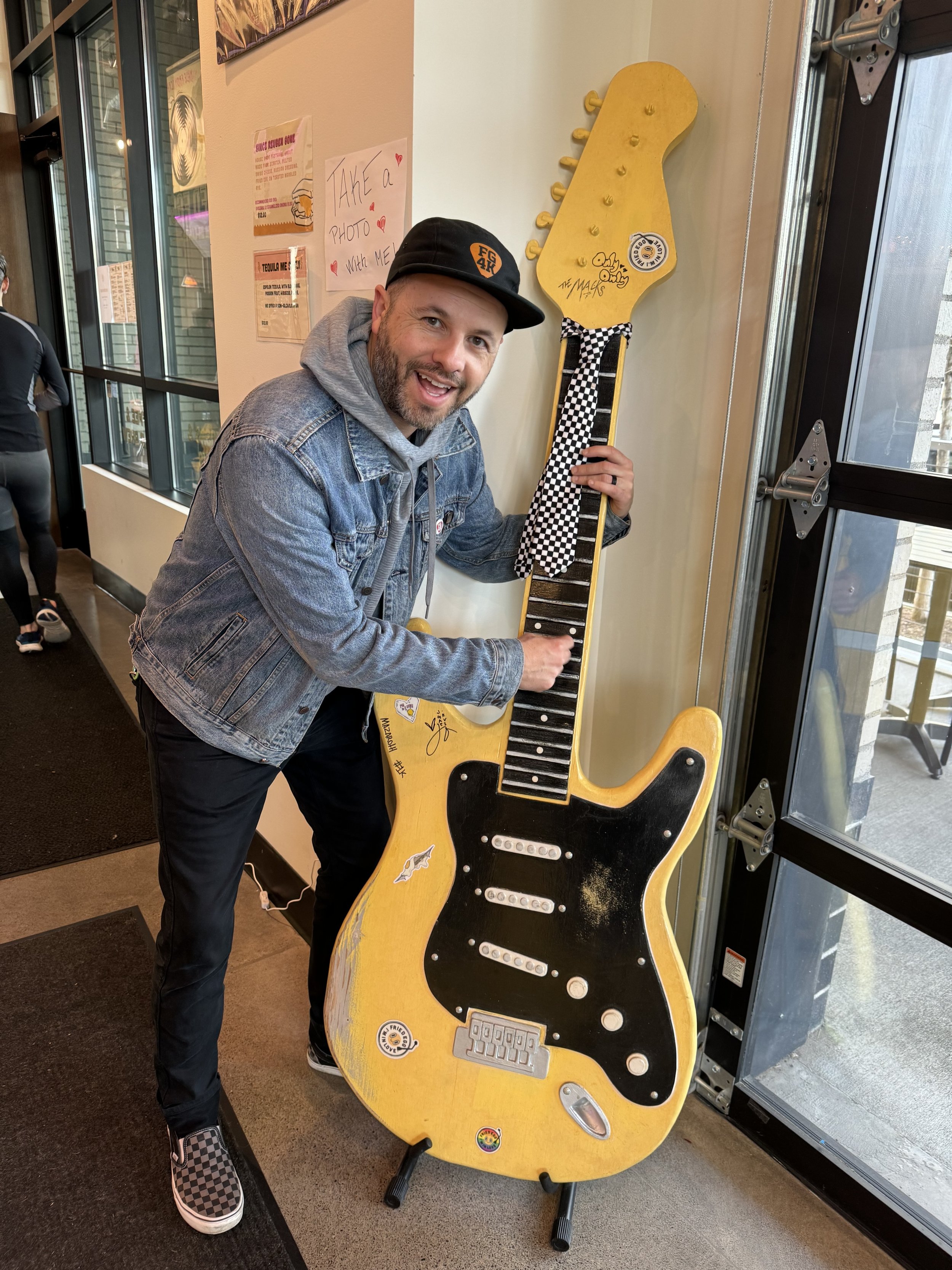 Ben Dudley, Executive Director of Free Guitars 4 Kids, posing playfully with an oversized guitar prop during a staff photo.