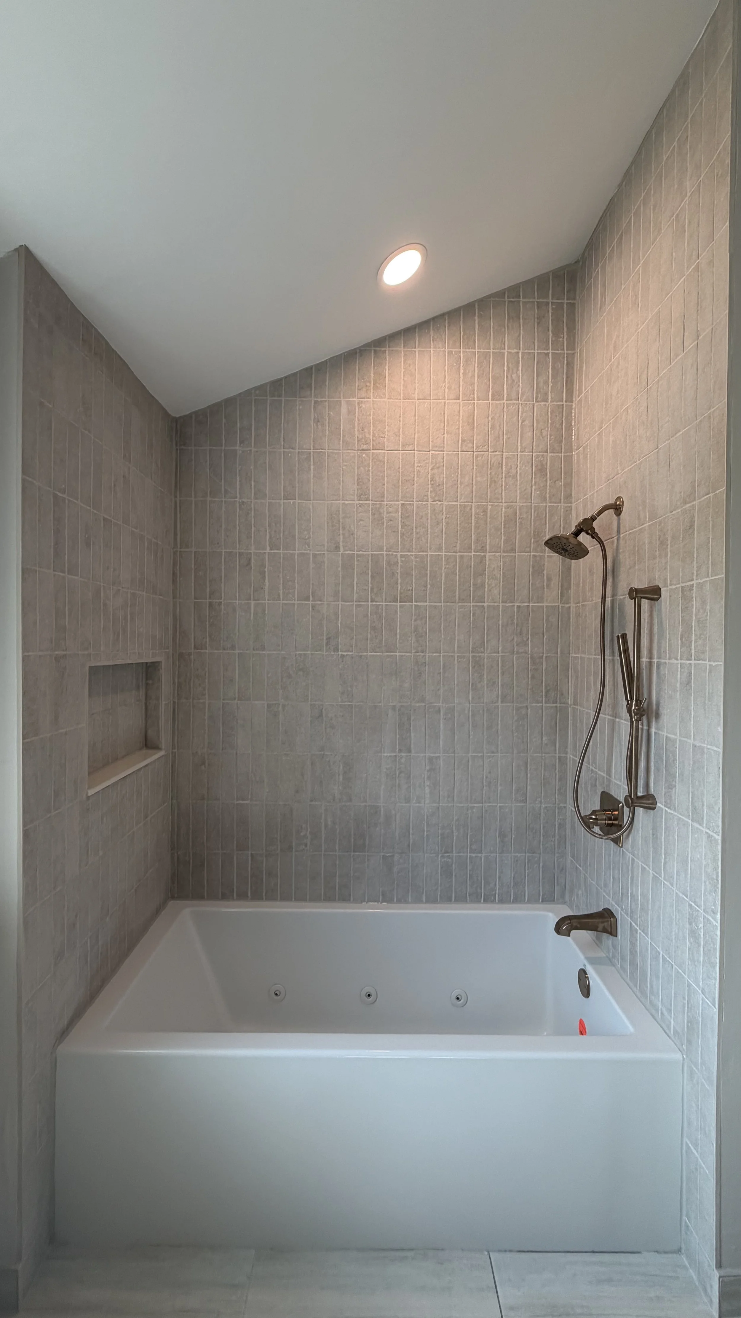 Bathroom shower with beige tiled walls, a built-in niche, a rain shower head, adjustable handheld shower, and a bathtub with jets.