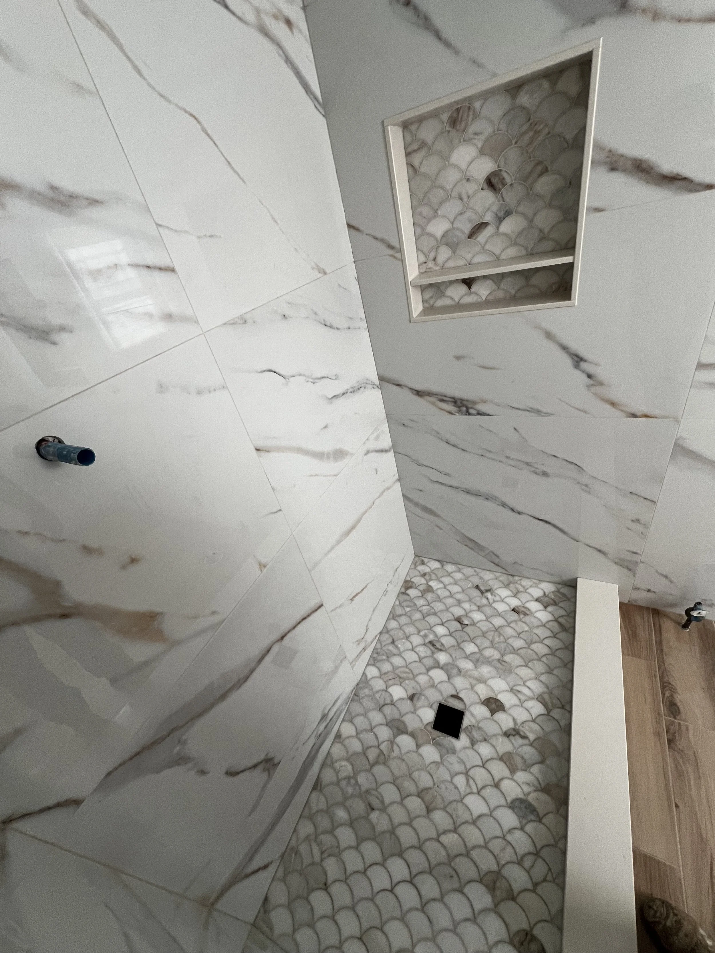 Bathroom with marble wall tiles, a niche with shell mosaic tiles, and patterned pebble floor tiles.