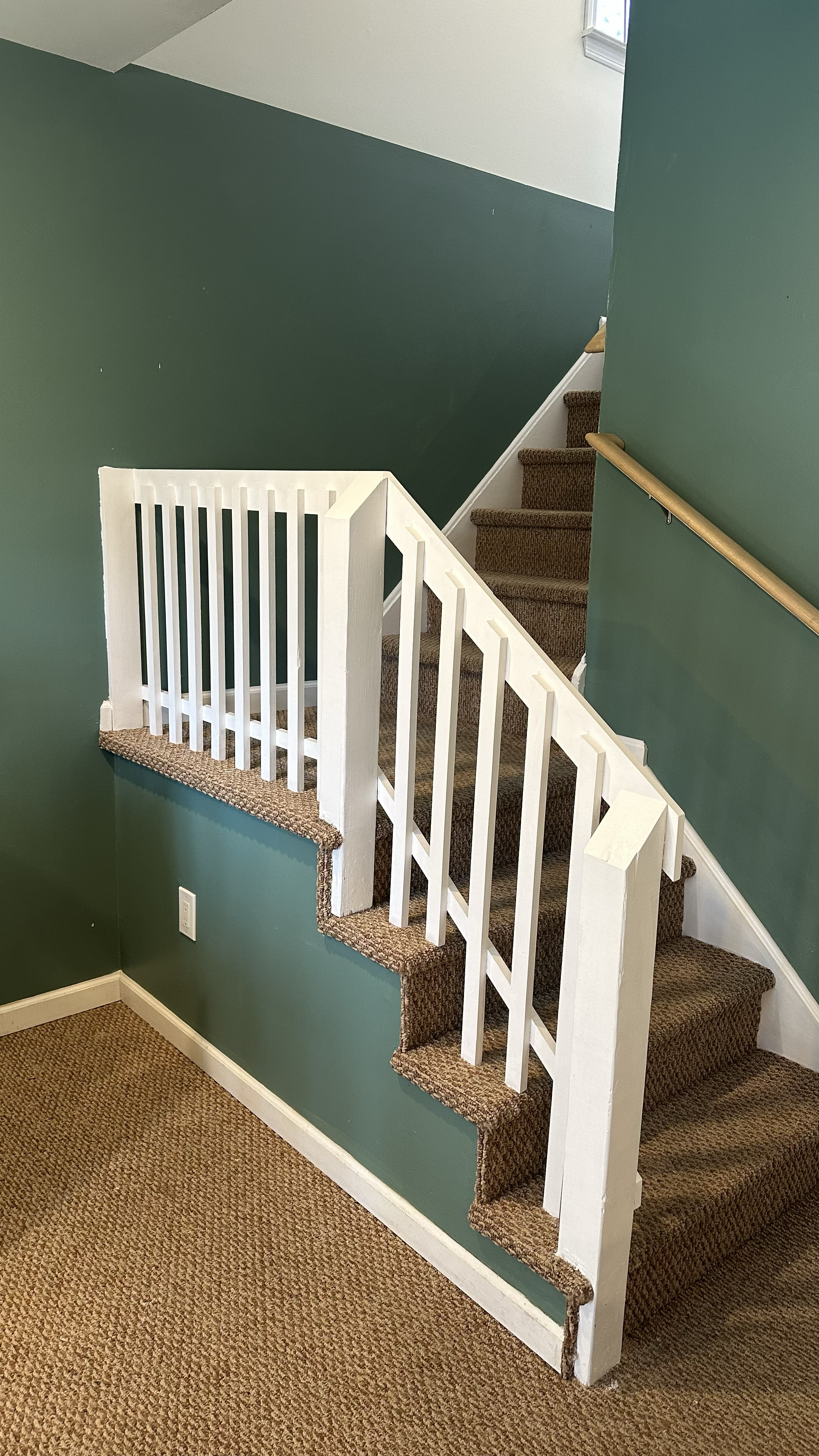 Image of a staircase with brown carpeted steps, a white balustrade on the side, and a green painted wall in a residential interior.