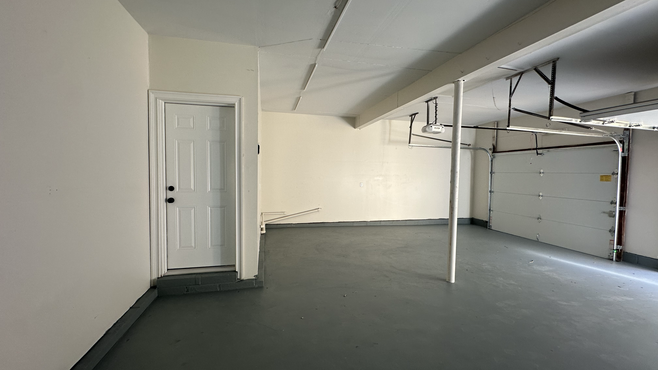 Empty garage with white walls, gray floor, a closed garage door, and a white door on the side.