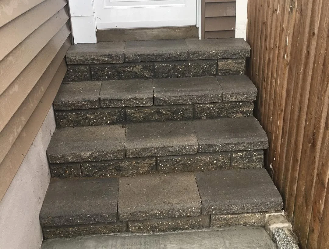 Concrete stairs leading up to a door, with a wooden fence on the right side and house siding on the left side.