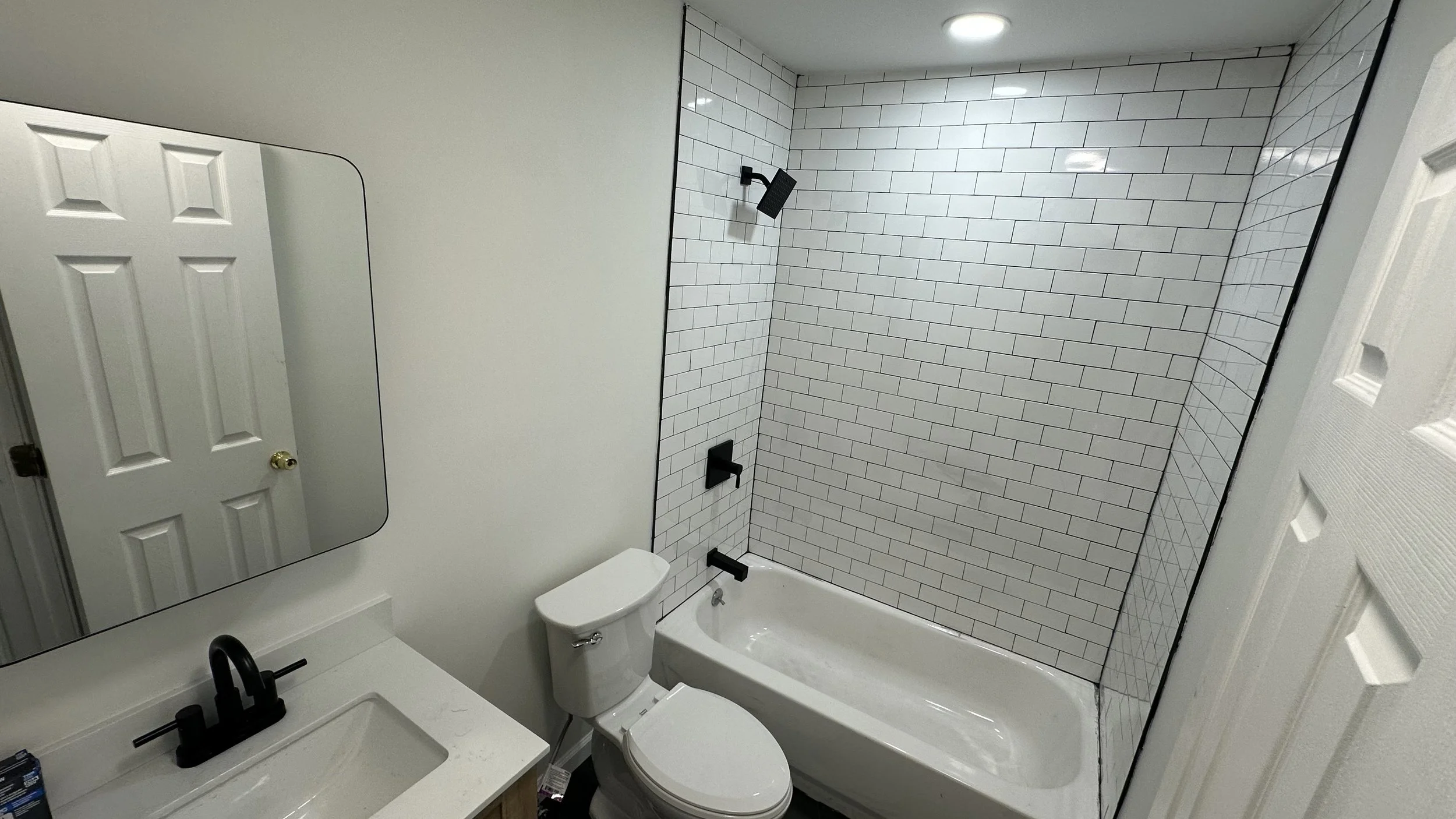 Bathroom with white subway tile shower, black fixtures, white toilet, and vanity with black faucet