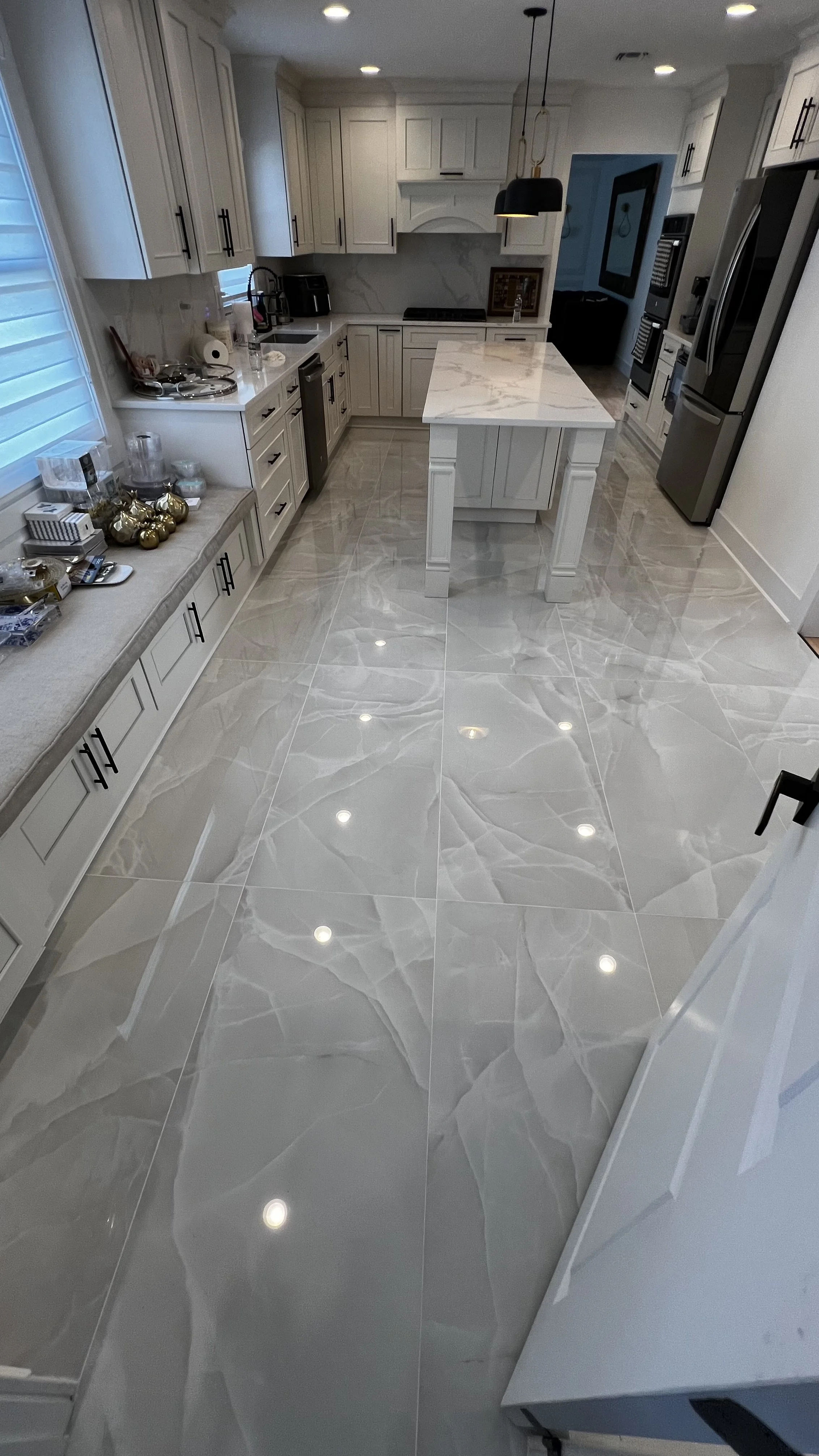 Modern kitchen with white cabinets, marble island, stainless steel appliances, and glossy marble floors with recessed lighting.