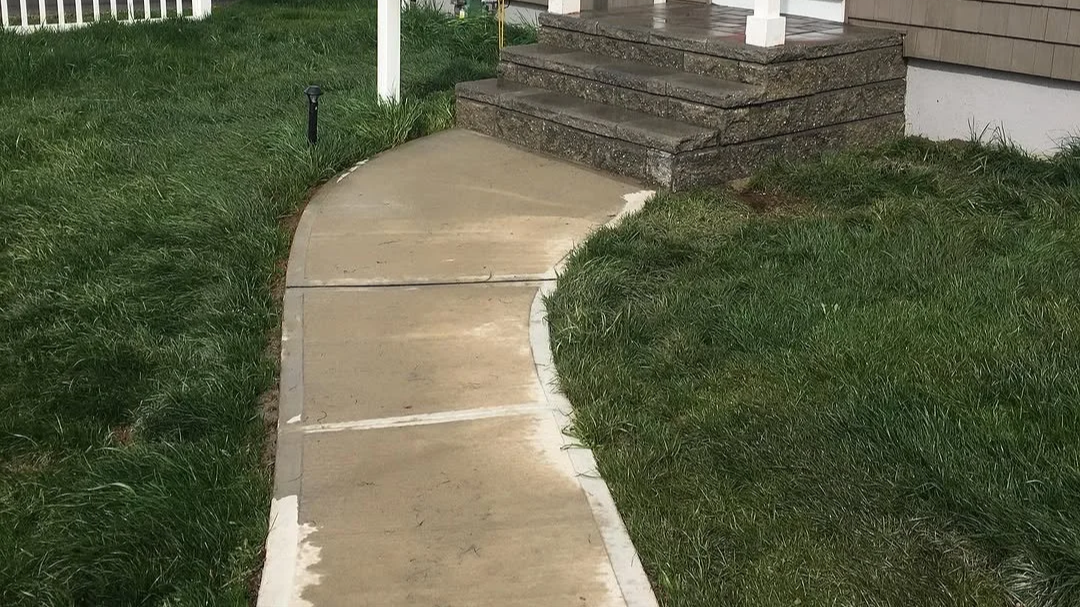 Concrete sidewalk curving towards house stairs with grass on both sides.