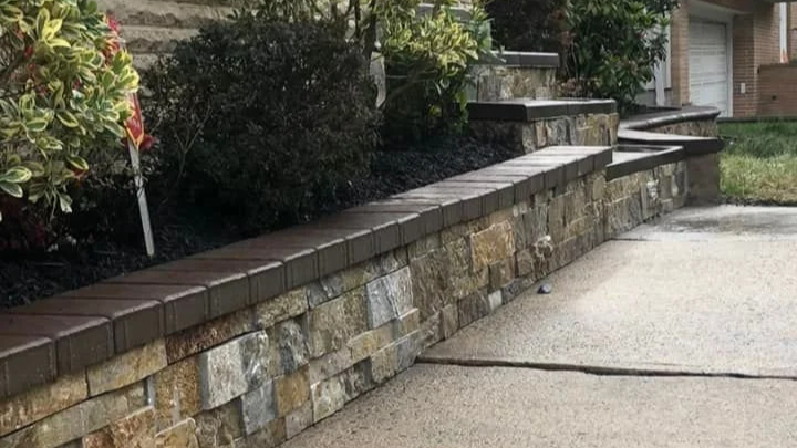Stone and brick retaining wall with leafless bushes in a landscaped yard.