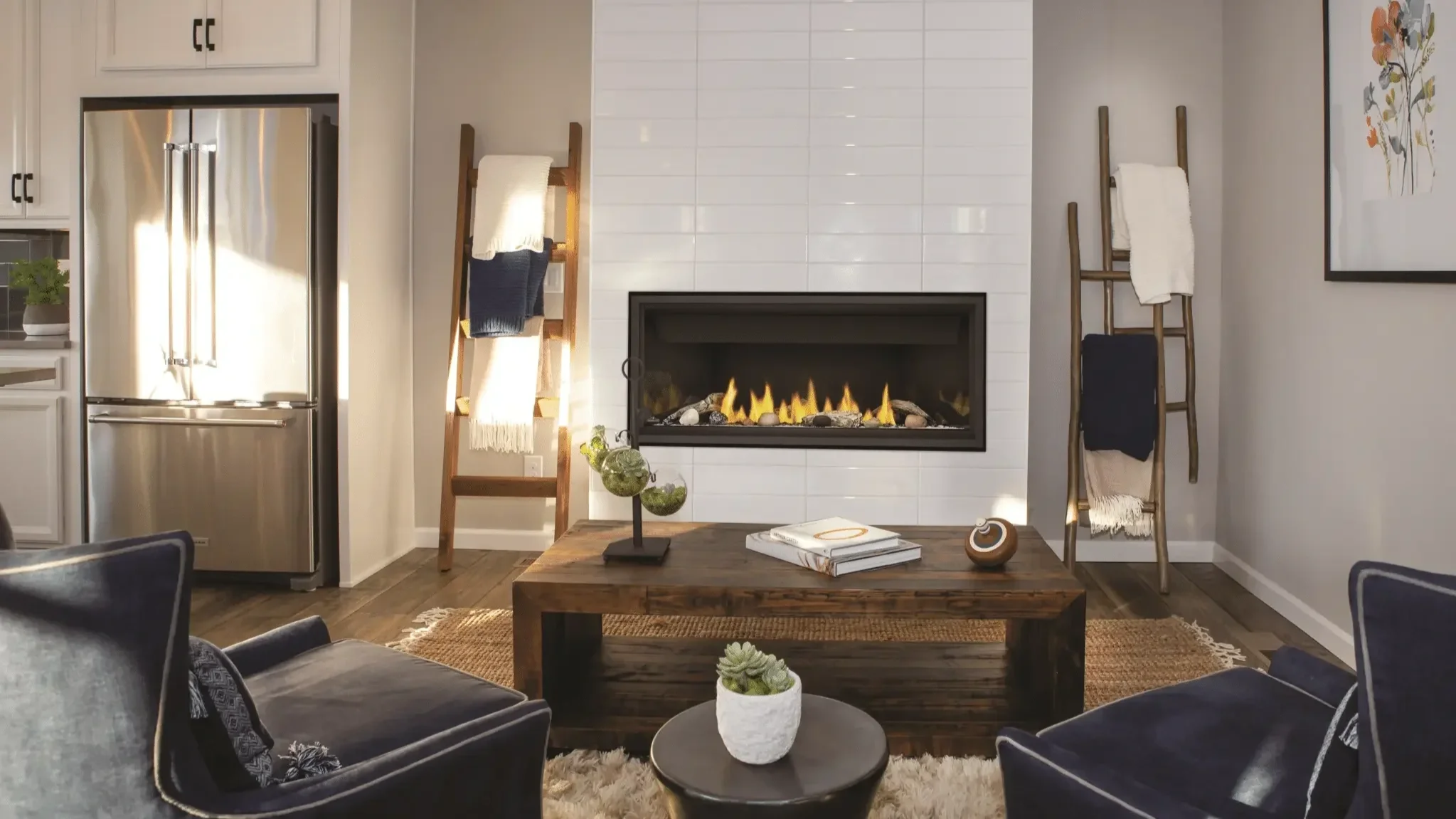 Living room with a modern gas fireplace, wooden ladder decor with blankets, a coffee table with books and decor, and dark armchairs, in a cozy home interior.