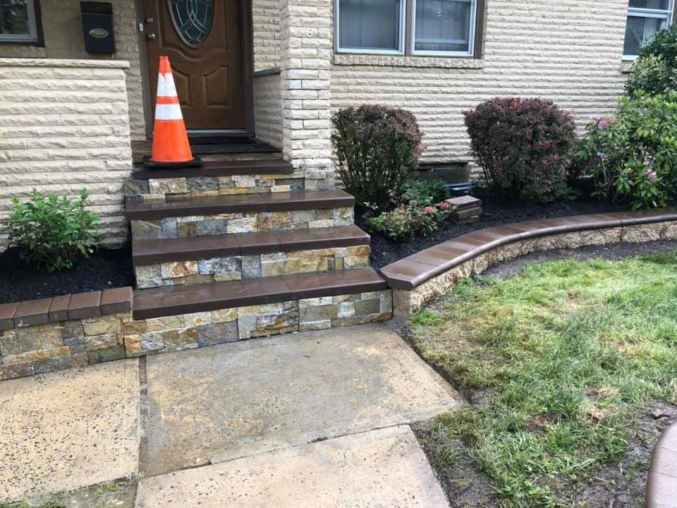 Front porch with stone steps, a traffic cone on top, and a garden bed with bushes and flowering plants.