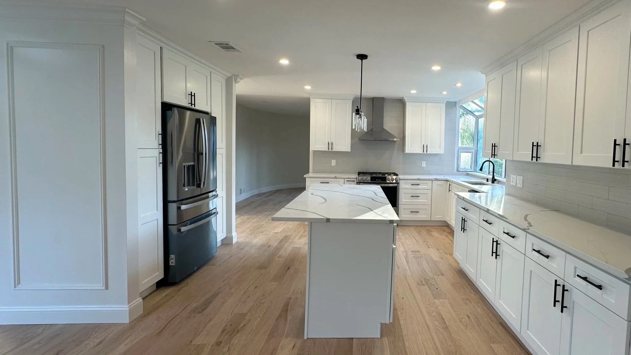 Modern kitchen with white cabinets, marble countertops, stainless steel refrigerator, gas stove, and a kitchen island.